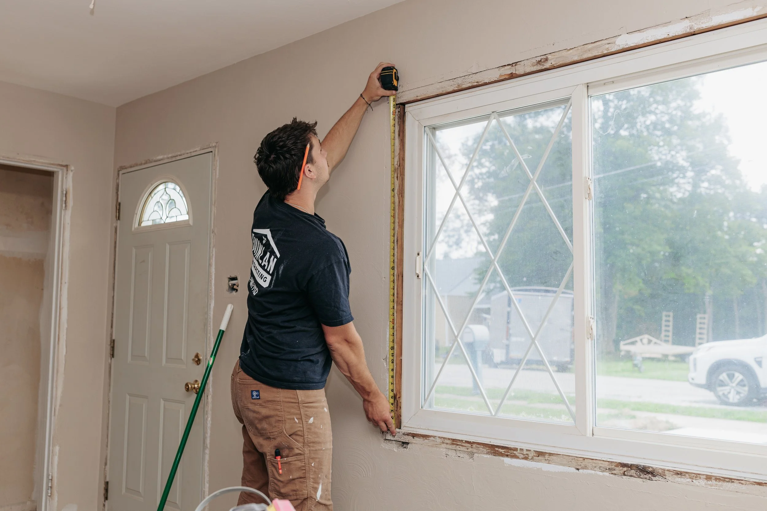 A man measuring the top frame of a window while working on home renovation inside a house.