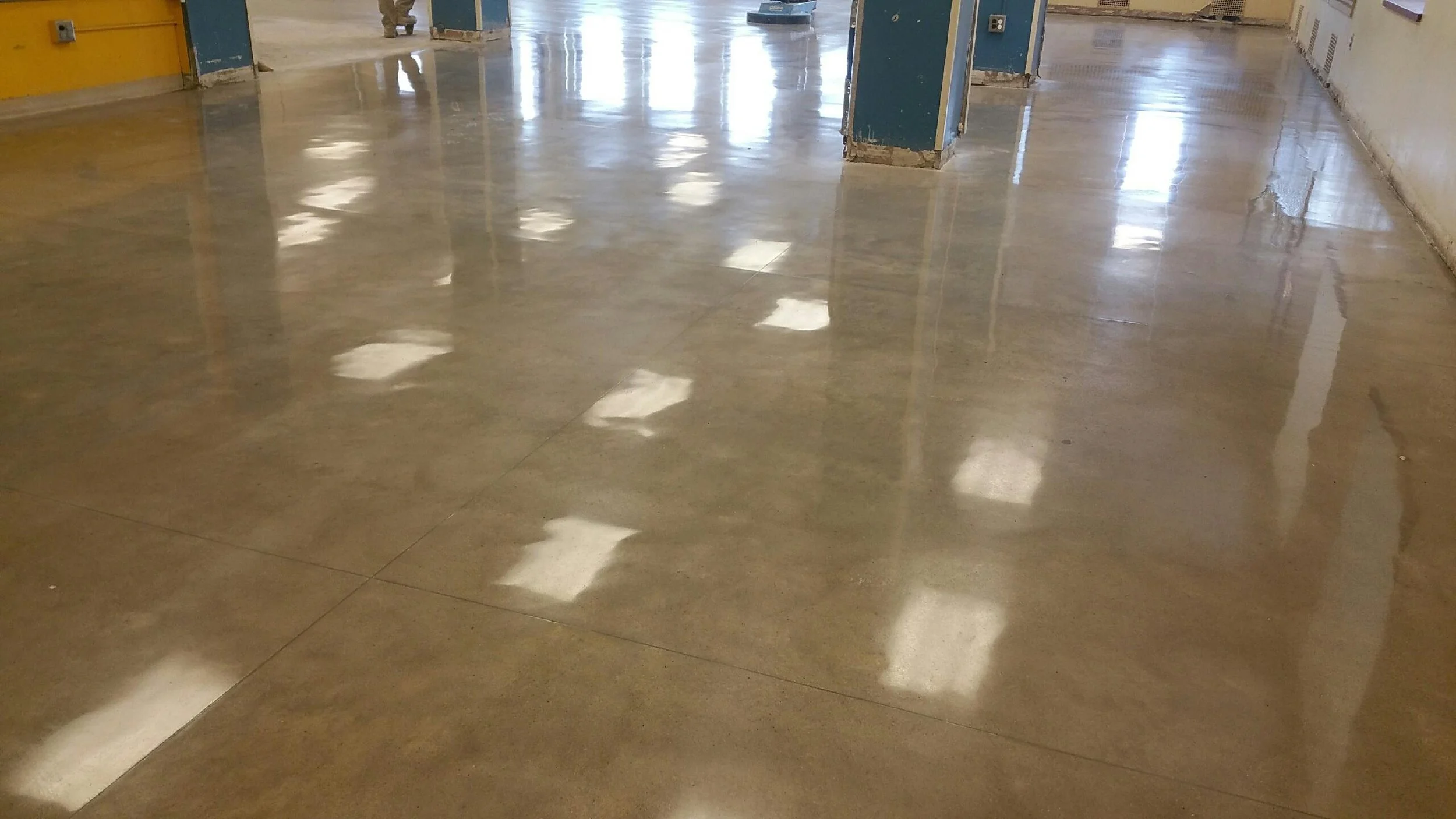 Polished concrete floor with reflections of ceiling lights in an indoor space, possibly under construction or renovation.