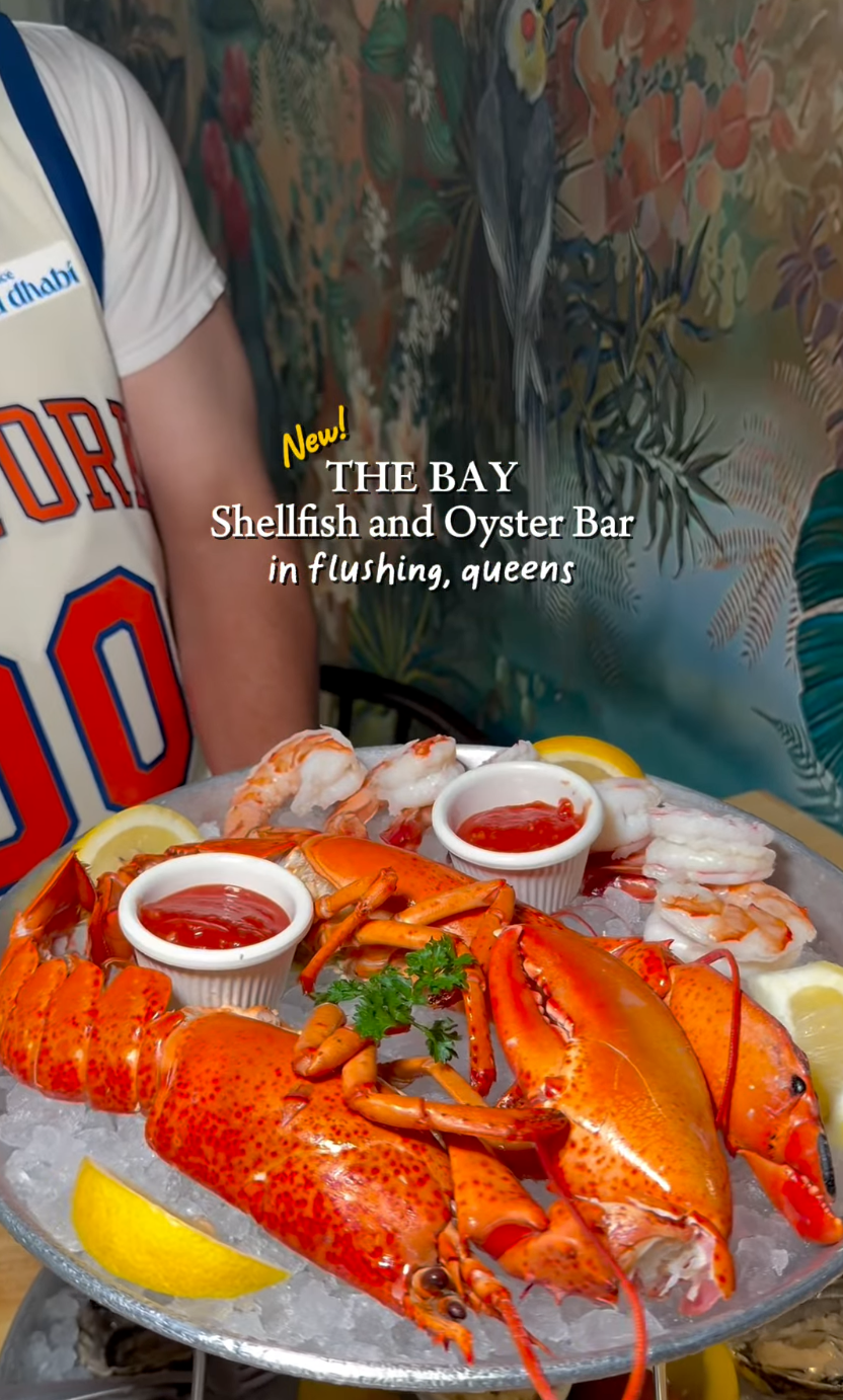 A seafood platter featuring lobster, shrimp, oysters, and shellfish on ice with lemon wedges, served with cocktail sauce at The Bay Shellfish and Oyster Bar in Queens.