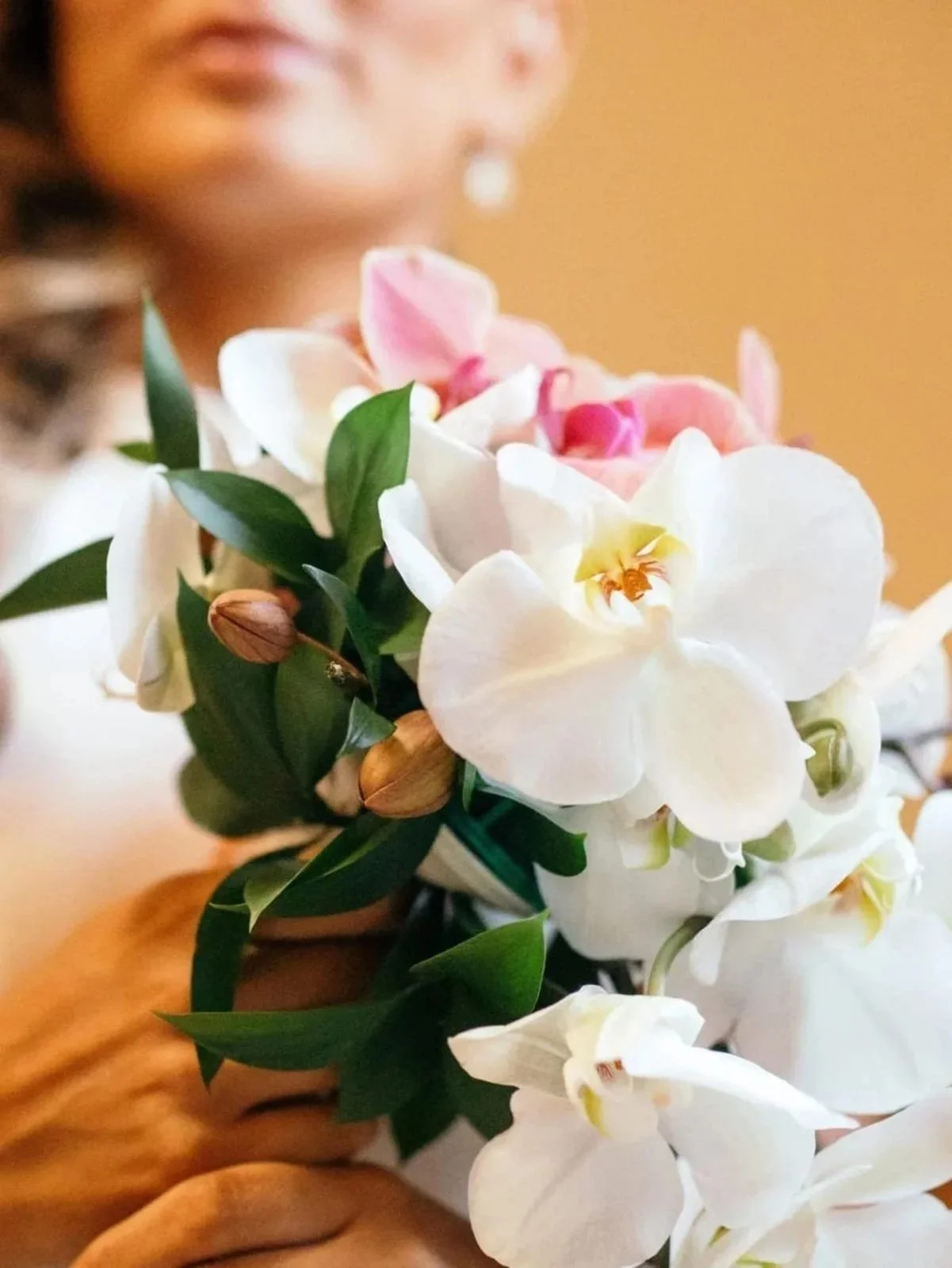 Ramo de flores con orquídeas blancas, rosa y verdes, siendo sostenido por una persona cuya cara no es claramente visible.
