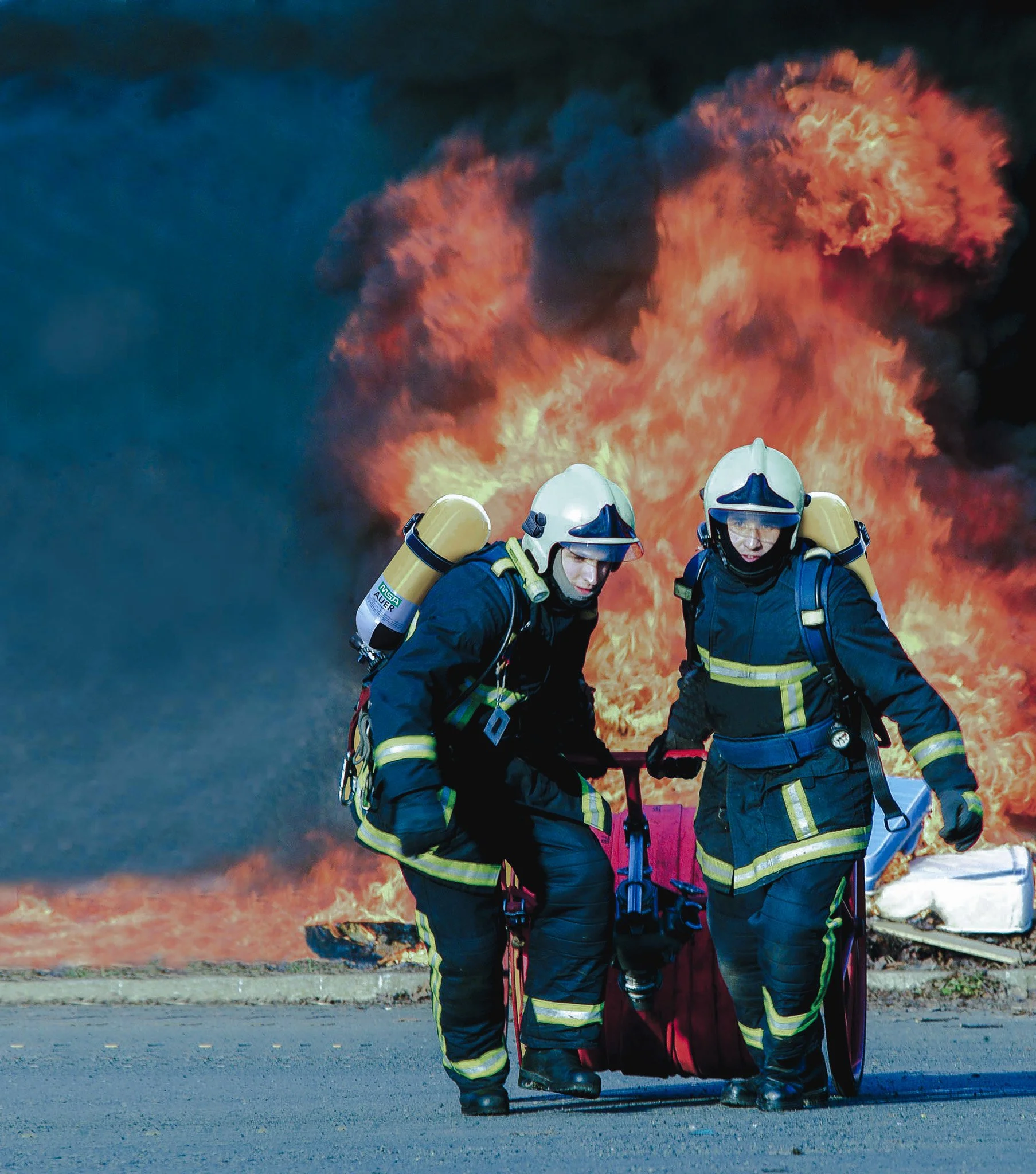 pompiers en tenue de lutte contre un incendie, portant des casques et équipements de protection, avec une explosion de feu et de fumée en arrière-plan.
