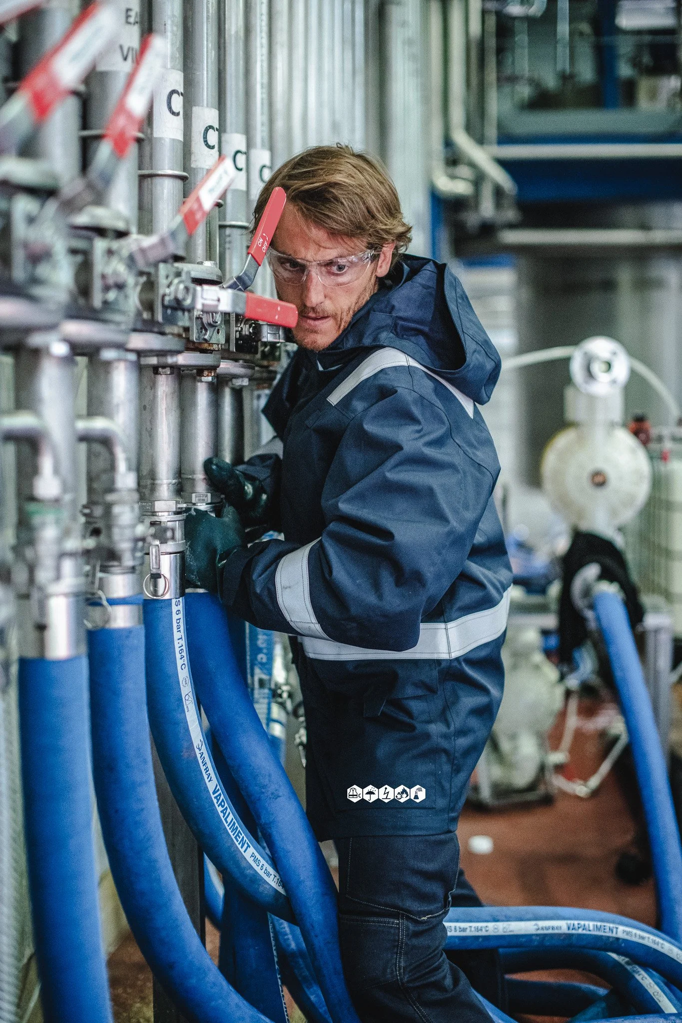 Un homme portant des lunettes de protection travaille avec des tuyaux bleus dans une usine.