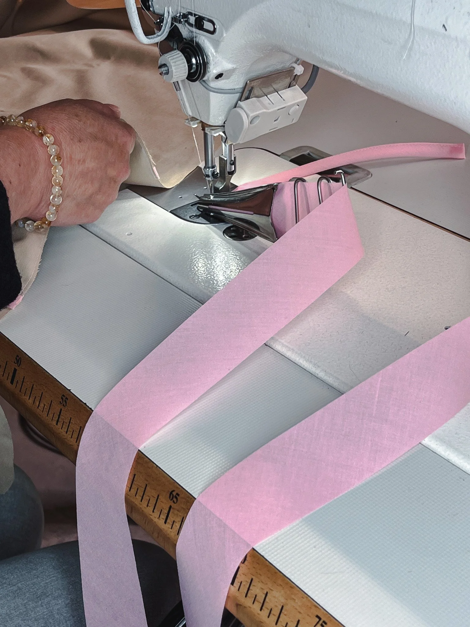 Une main cousant du tissu rose à une machine à coudre sur une table en bois.