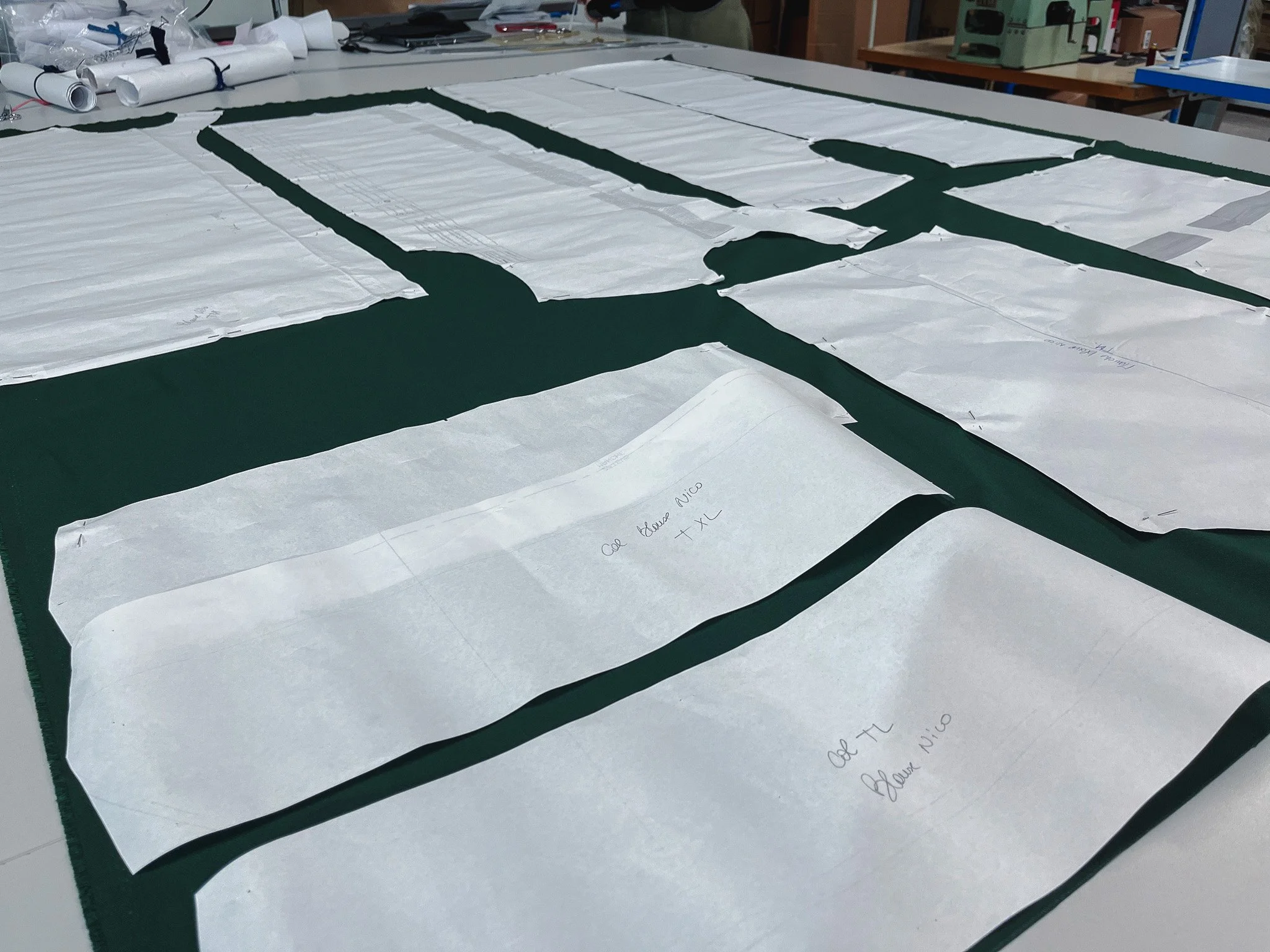Plusieurs plans ou esquisses de vêtements ou tissus, étalés sur une table de travail, dans un atelier ou un studio de couture.