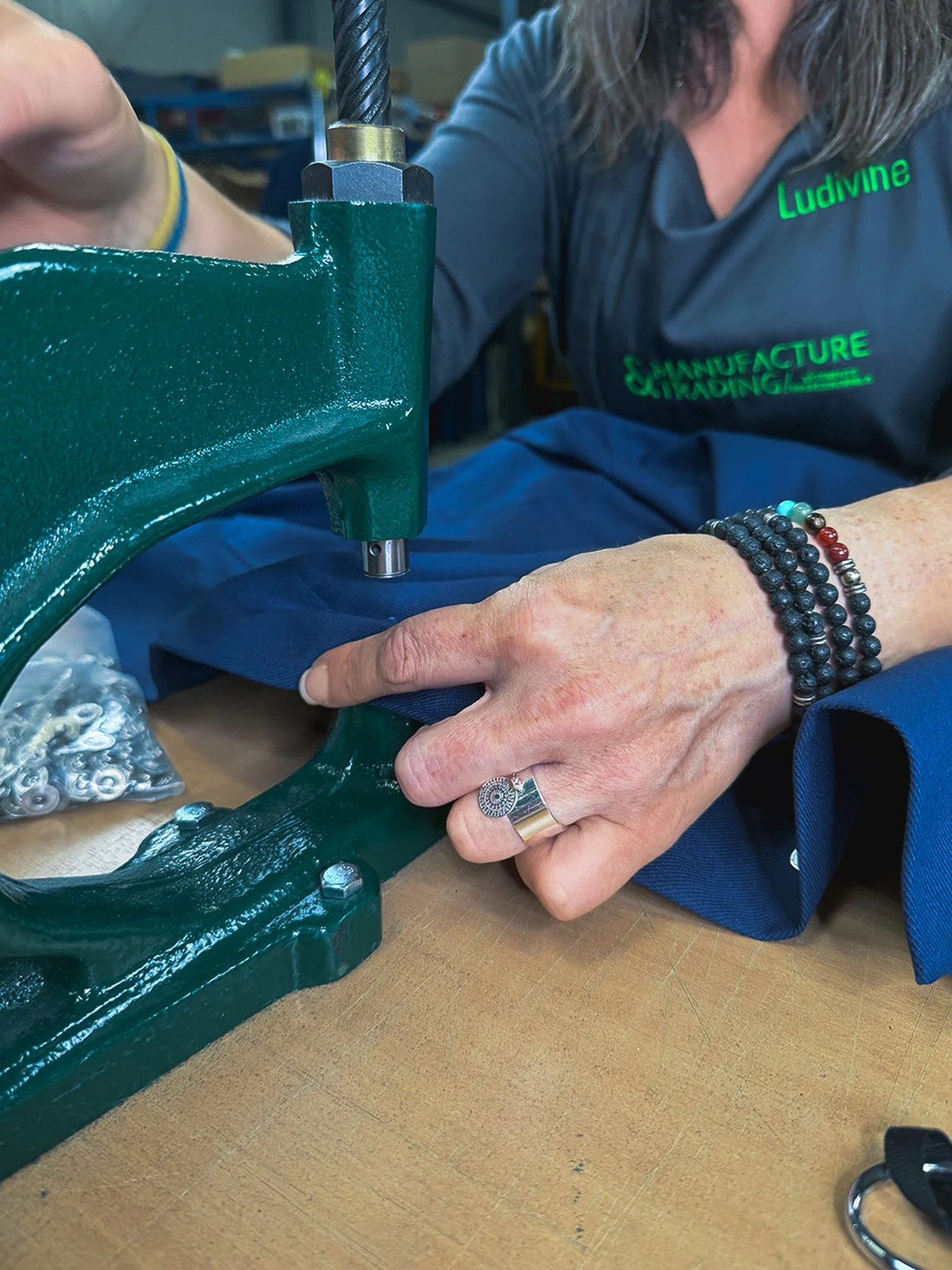 Une personne ajuste une pièce d'une machine ou d'un équipement industriel en utilisant ses mains, portant plusieurs bracelets et une bague, avec un fond d'atelier ou de laboratoire.
