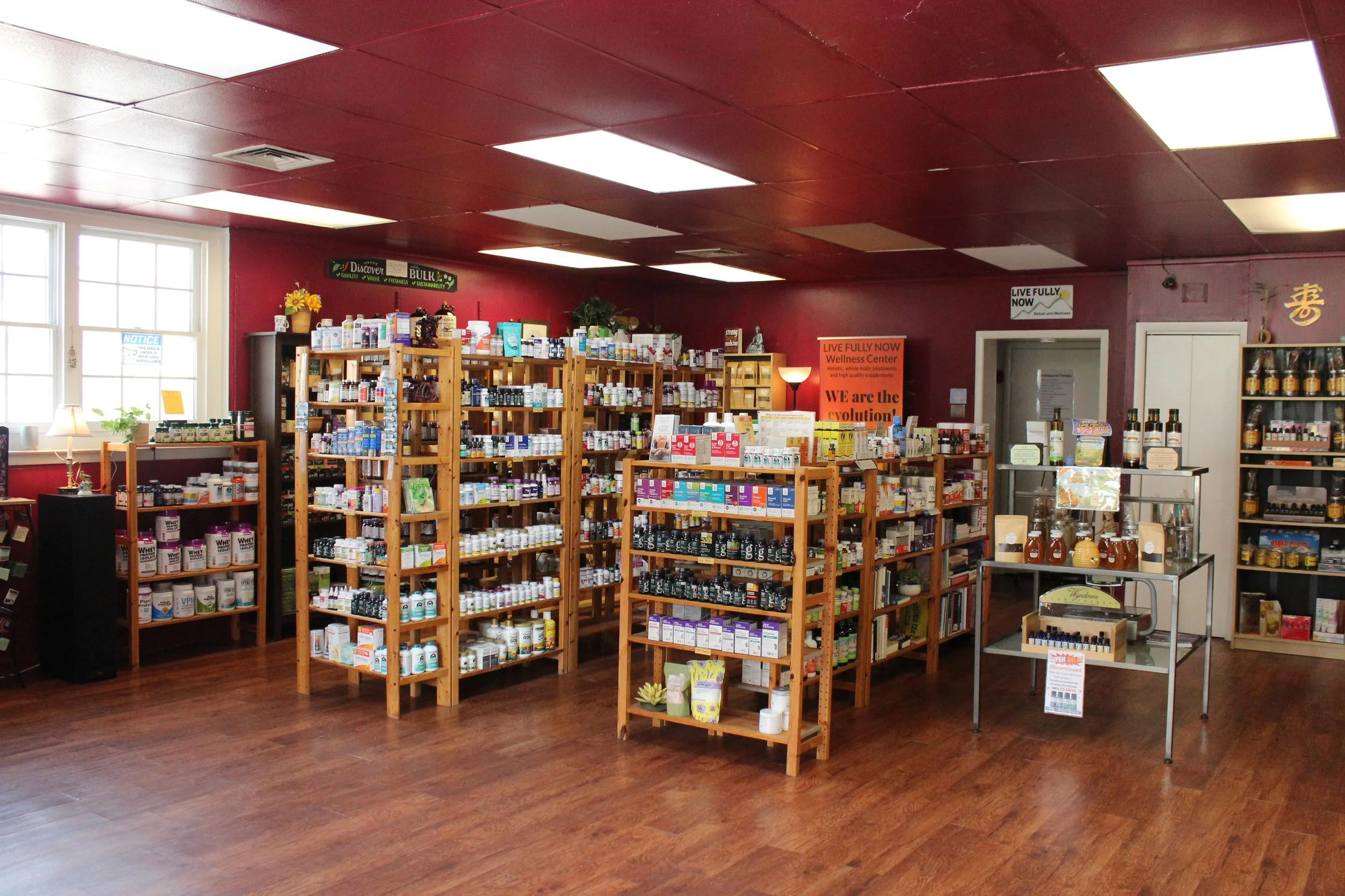 Interior of a wellness or supplement store with wooden shelves stocked with various bottles and containers, large windows letting in natural light, and signs on the walls promoting health and wellness.
