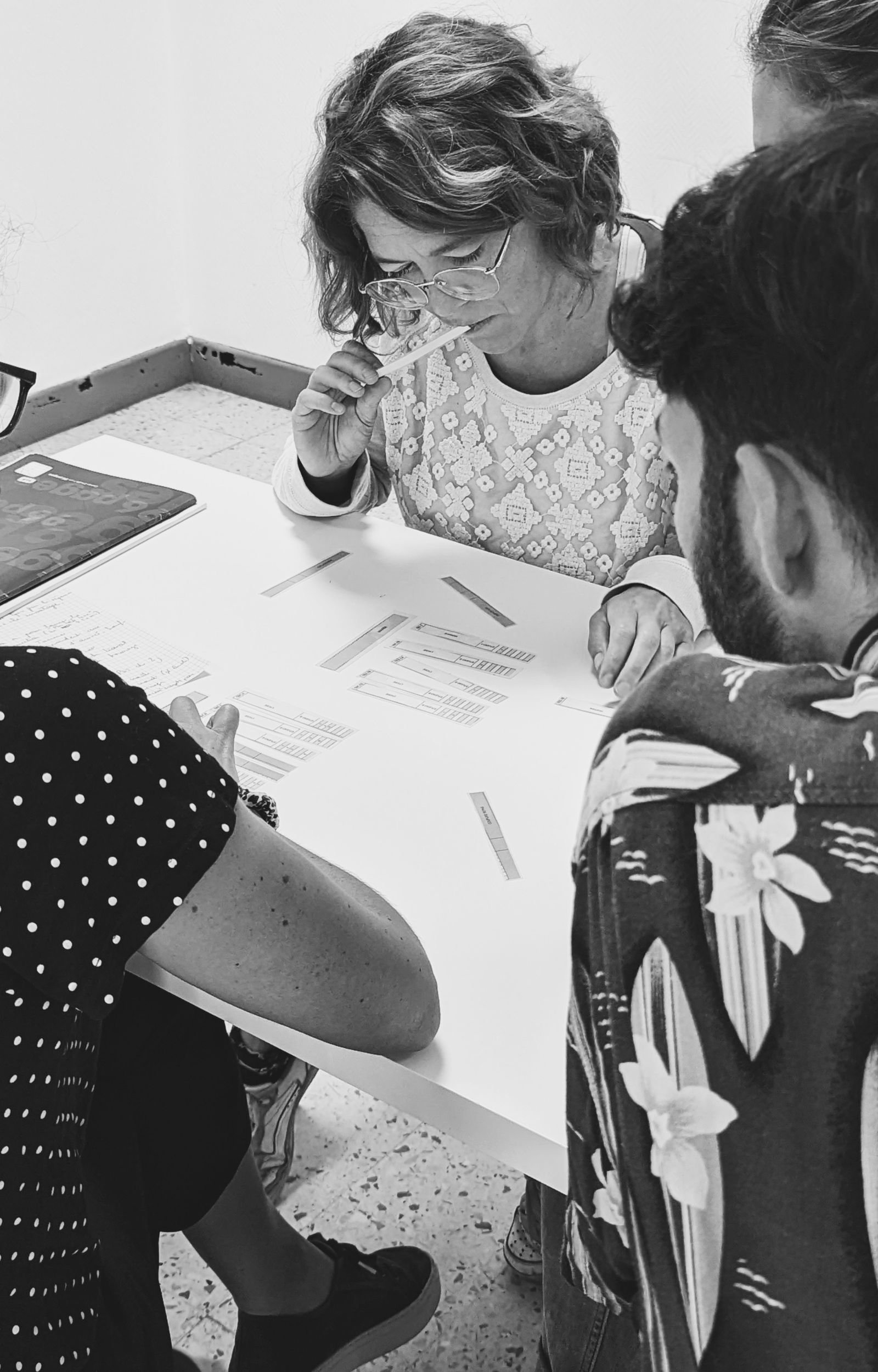 Groupe de trois personnes assises autour d'une table, étudiant des documents et des graphiques, en discussion, dans une ambiance de travail