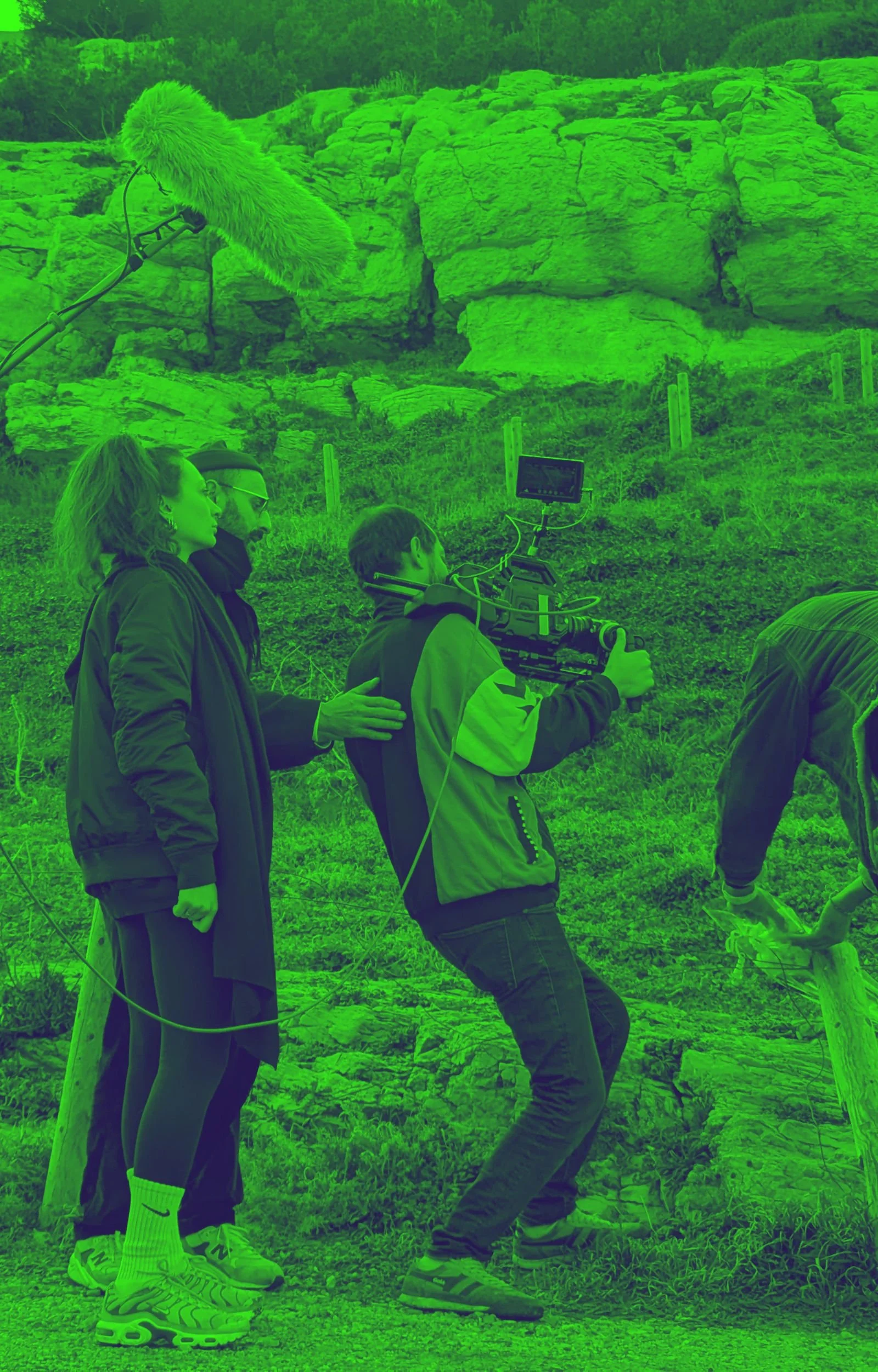 Une équipe de tournage filme un animal dans un paysage rocheux et verdoyant.
