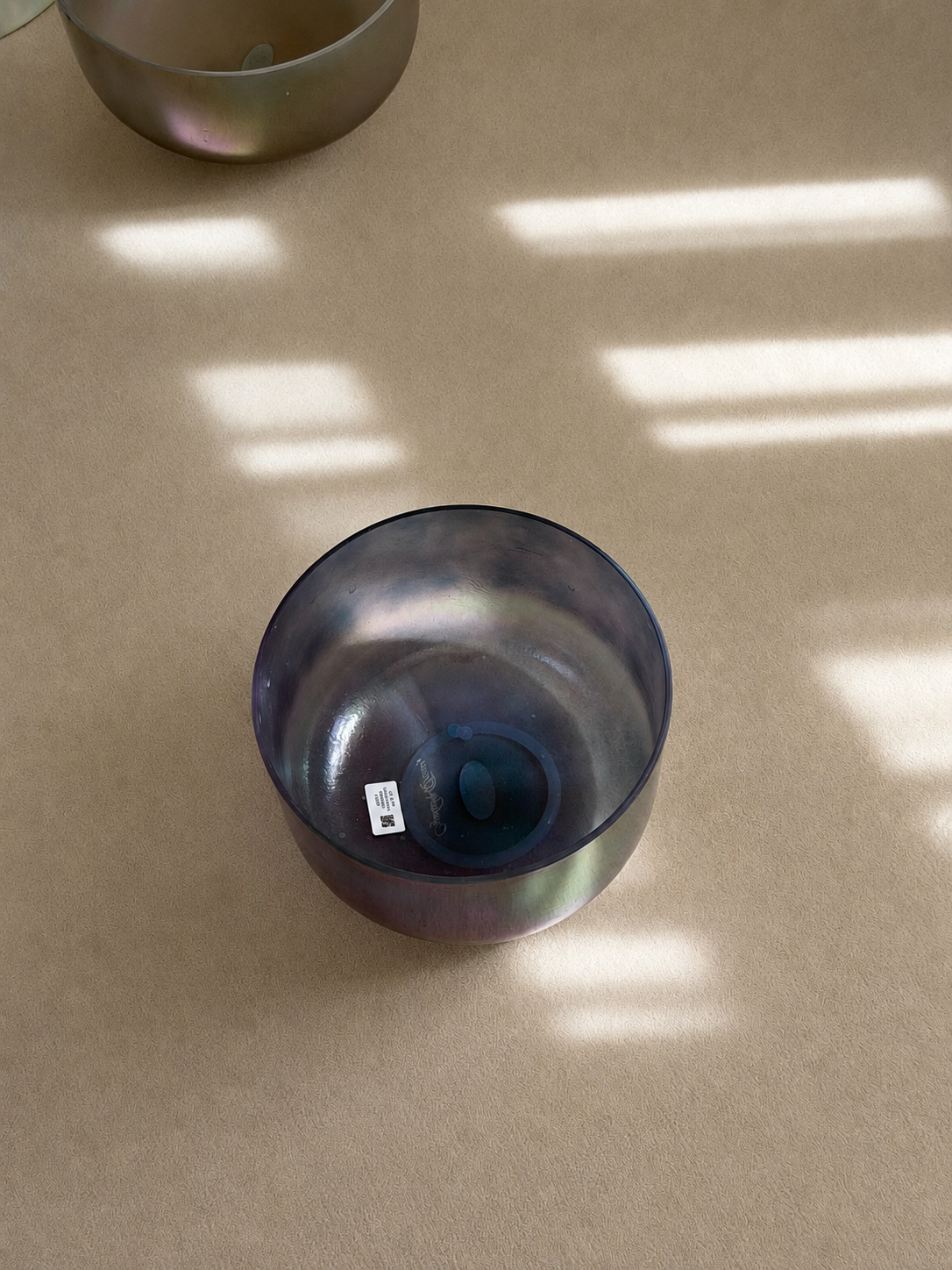 Two metal singing bowls placed on a beige surface with sunlight and shadow patterns.