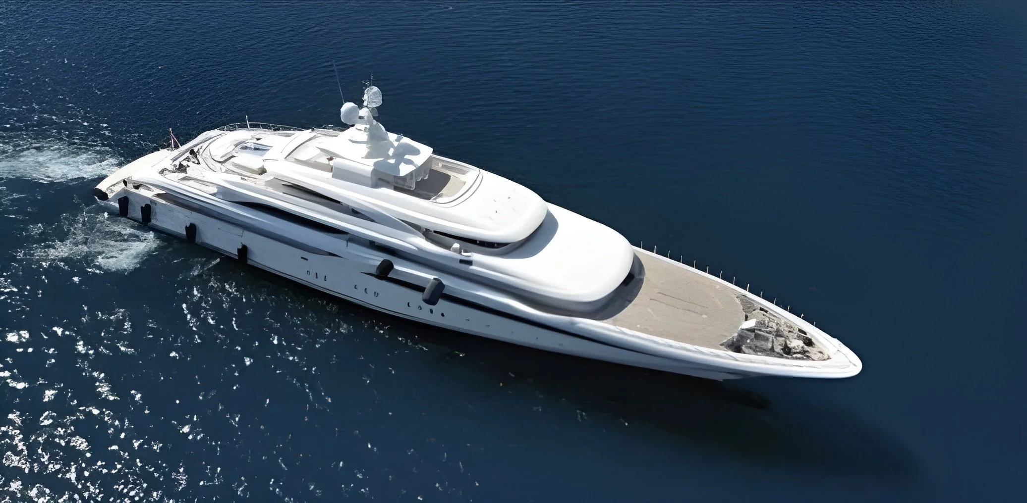 A white luxury yacht sailing on dark blue ocean water, viewed from above.