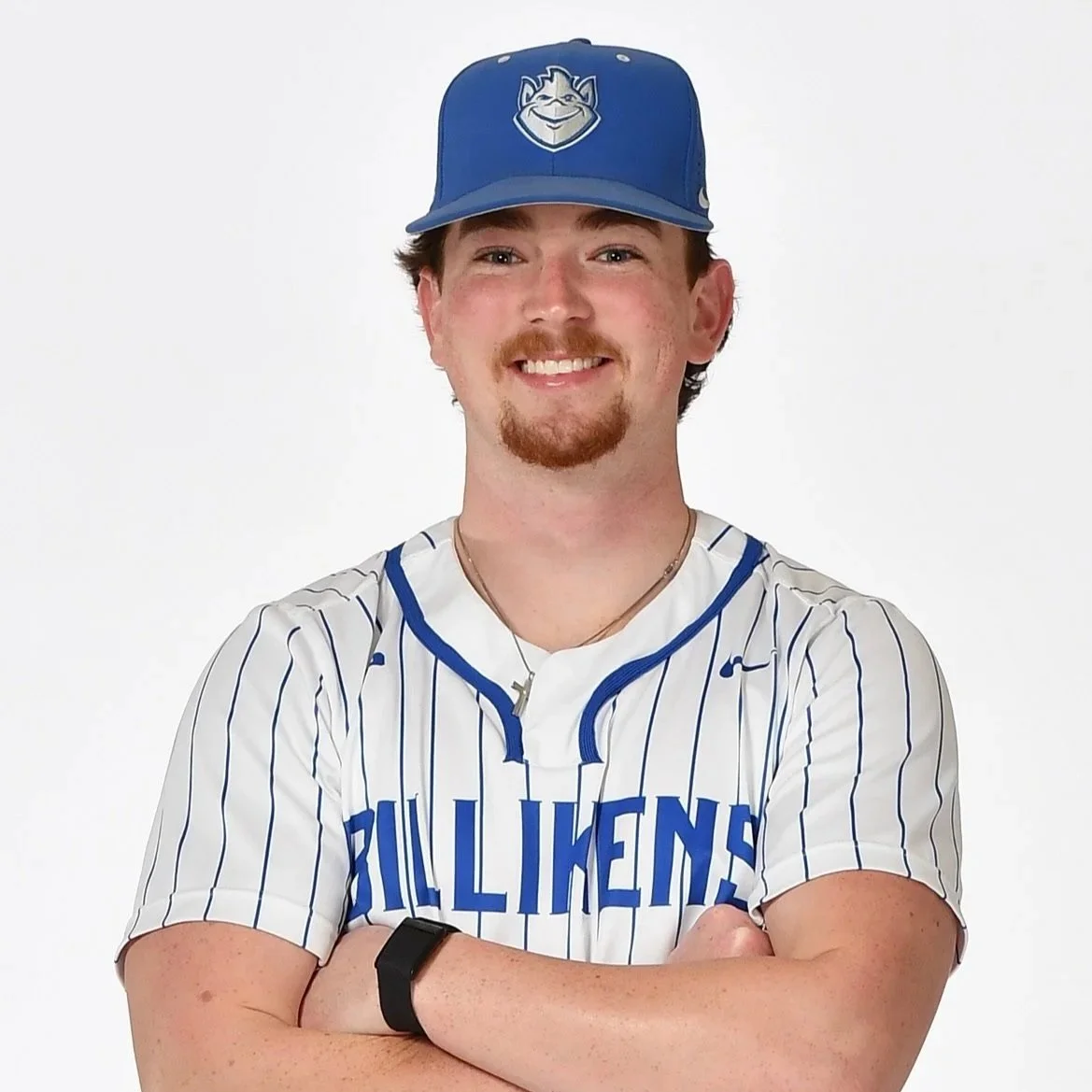 Young man in a baseball cap and jersey, smiling with arms crossed, standing against a white background.