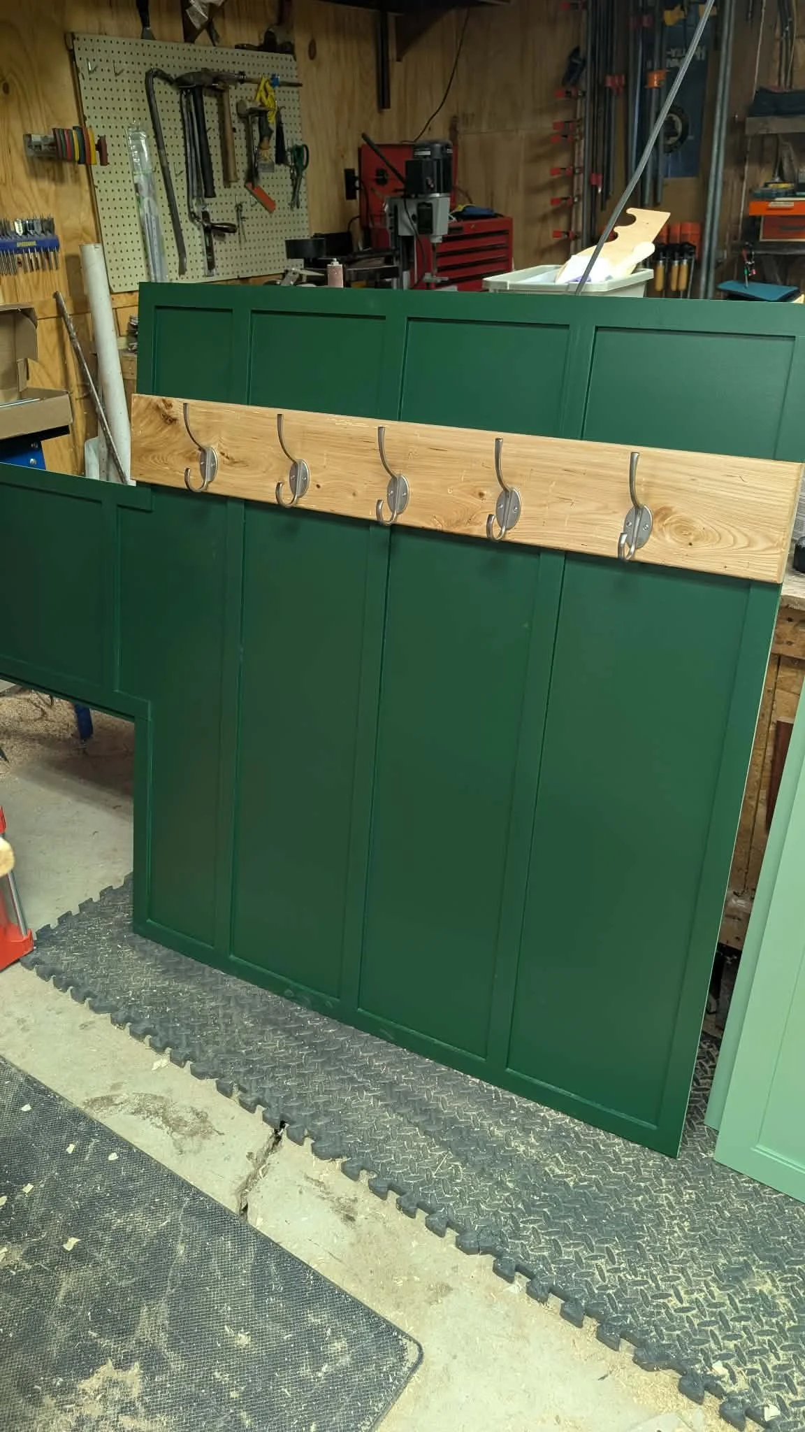 Dark green mudroom back panel with wood coat hooks