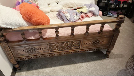 Antique wood footboard with carved panels, turned posts, and spindles before the bench conversion.