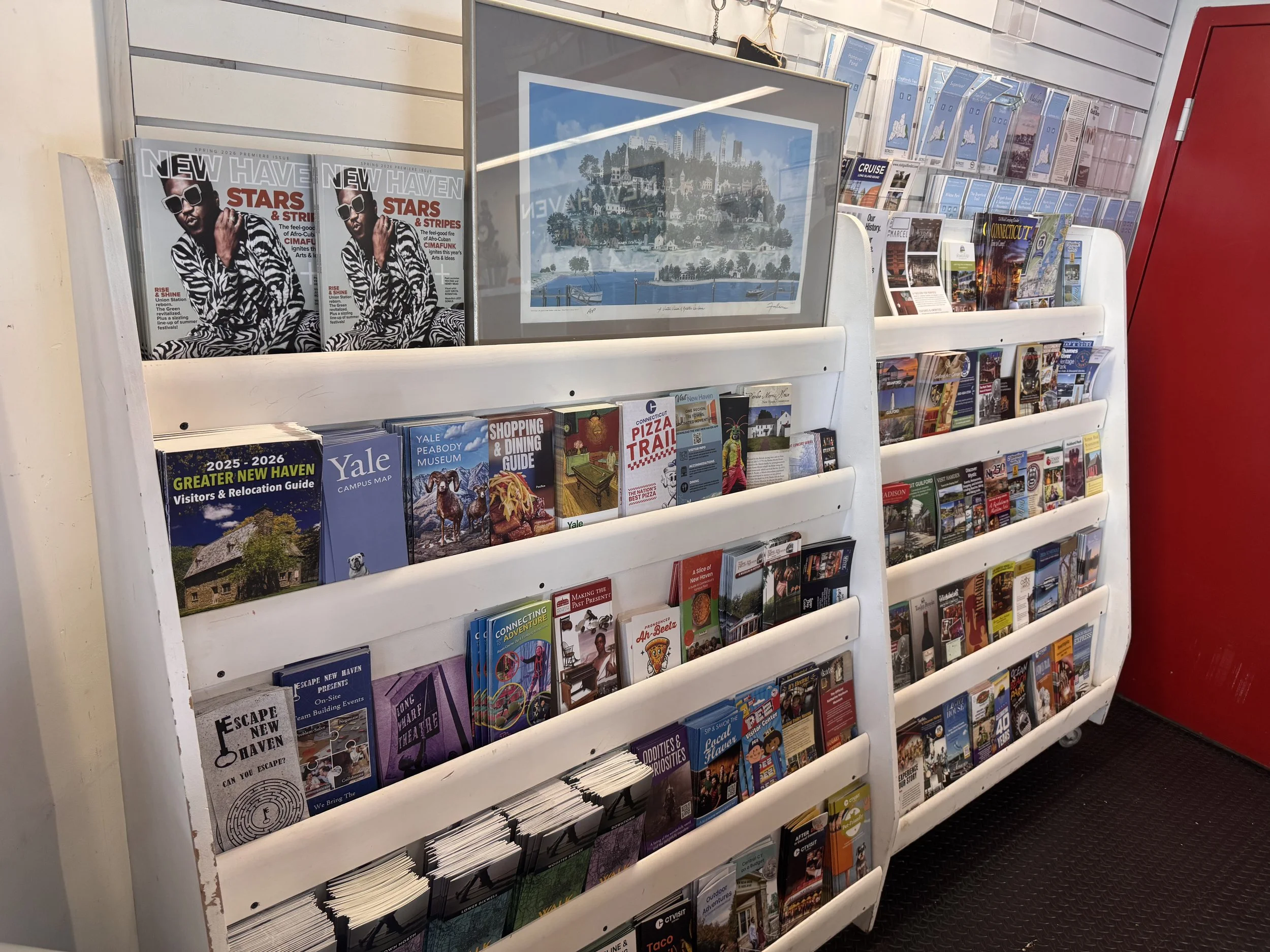 Display of various tourist and local brochures and magazines on white rack, including a New Haven magazine, Yale brochure, and travel guides.