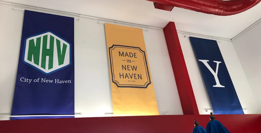 Three banners hanging from the ceiling, the first with 'NHV' and 'City of New Haven', the second with 'Made in New Haven', and the third with a large letter 'Y'.