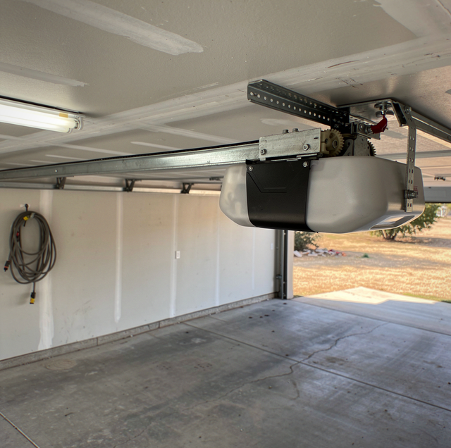 Interior of a garage with white walls, concrete floor, mounted garage door opener system with metal rails, and rope coil on t
