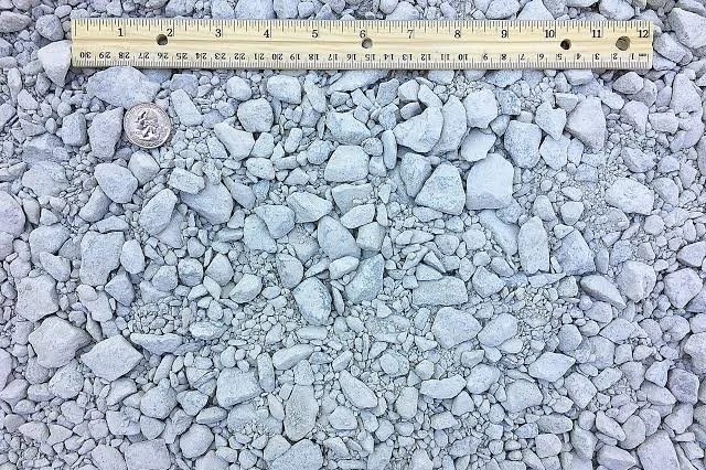 Grayscale gravel surface with small rocks and stones, a wooden ruler at the top, and a quarter coin to the left for scale.