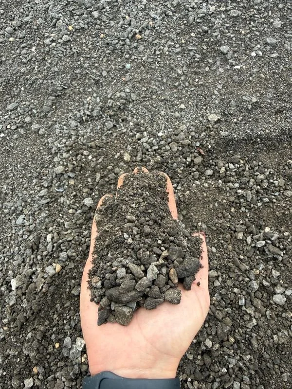 Person holding a handful of dark asphalt millings that have been recycled.