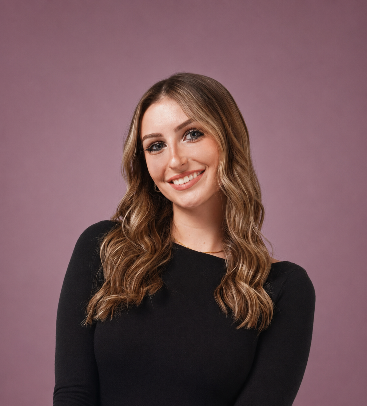 A woman with long wavy brown hair, blue eyes, and light skin, smiling and wearing a black top, against a purple gradient background.