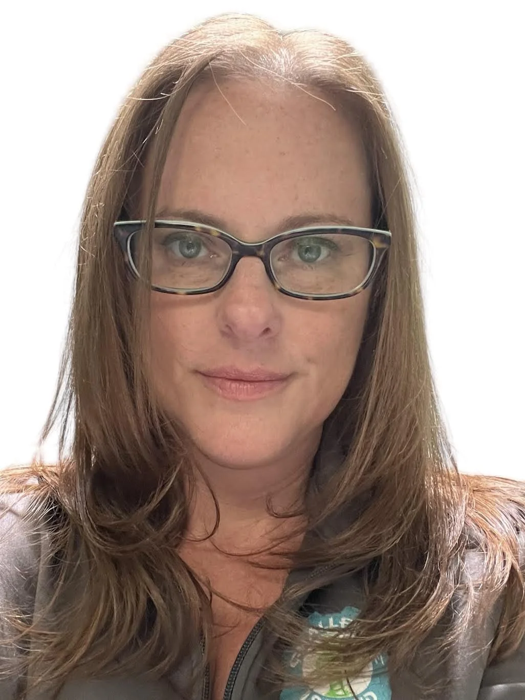 A woman with long brown hair and glasses, looking directly at the camera, wearing a zipped jacket.