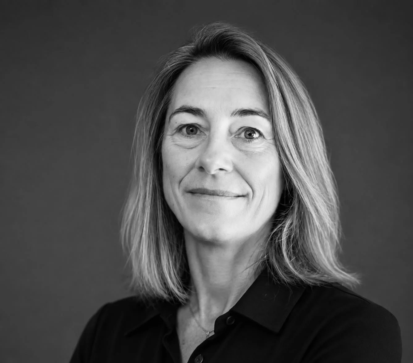 Black and white portrait of a woman with shoulder-length hair, wearing a dark collared shirt, smiling gently, against a plain backdrop.
