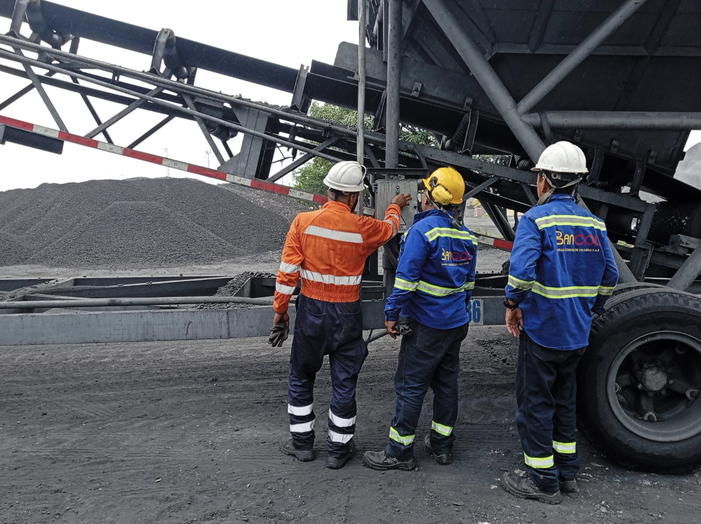 Tres trabajadores con cascos, uno de ellos ajustando una máquina en una cantera de carbón, servicio bancol.