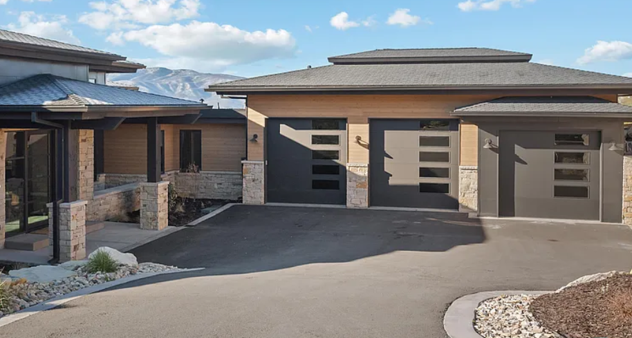 Modern house with three garage doors, a stone and wood exterior, and a driveway leading up to it.