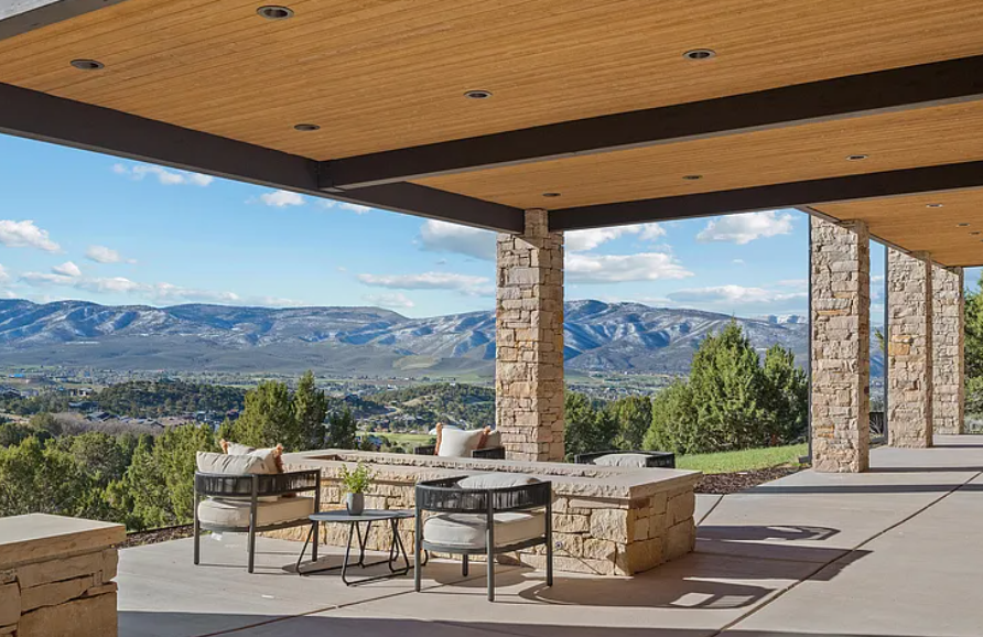 Outdoor patio with stone columns, seating area, and a scenic mountain view under a wooden ceiling.