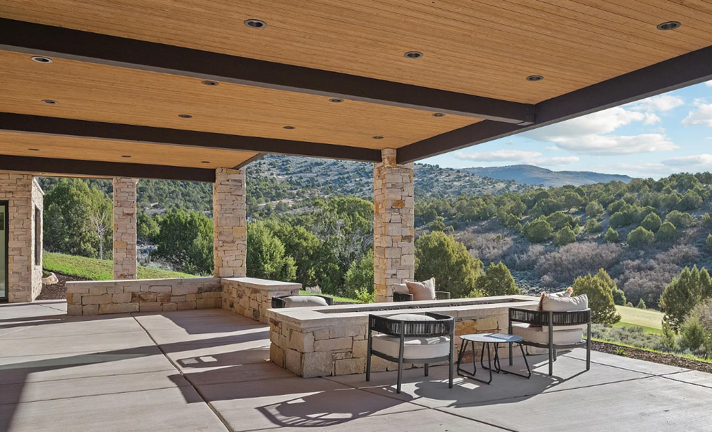 Covered patio with stone columns and seating area overlooking a lush green landscape with trees and hills in the background.