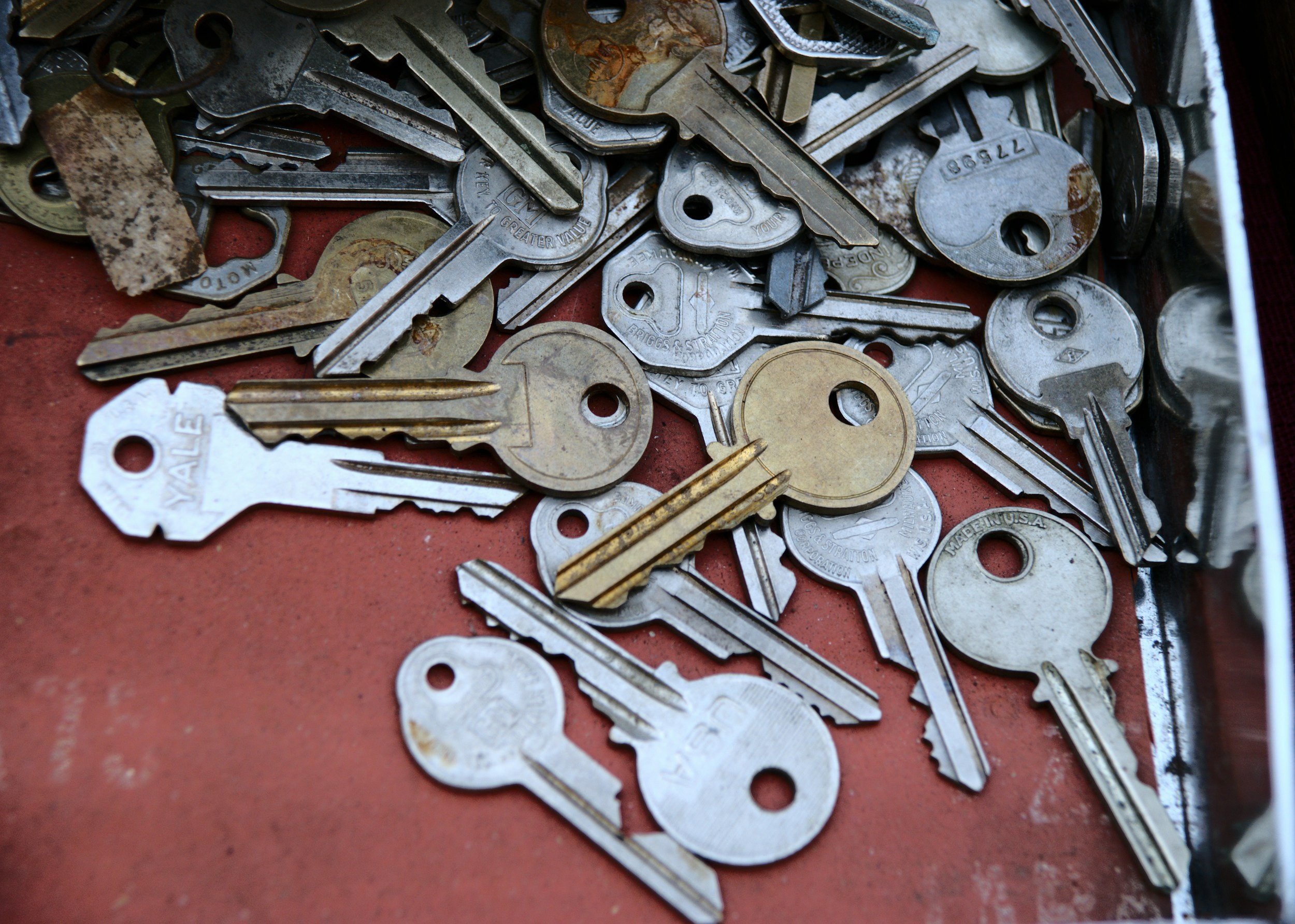 A collection of various keys, some rusted and some shiny, scattered on a red surface.
