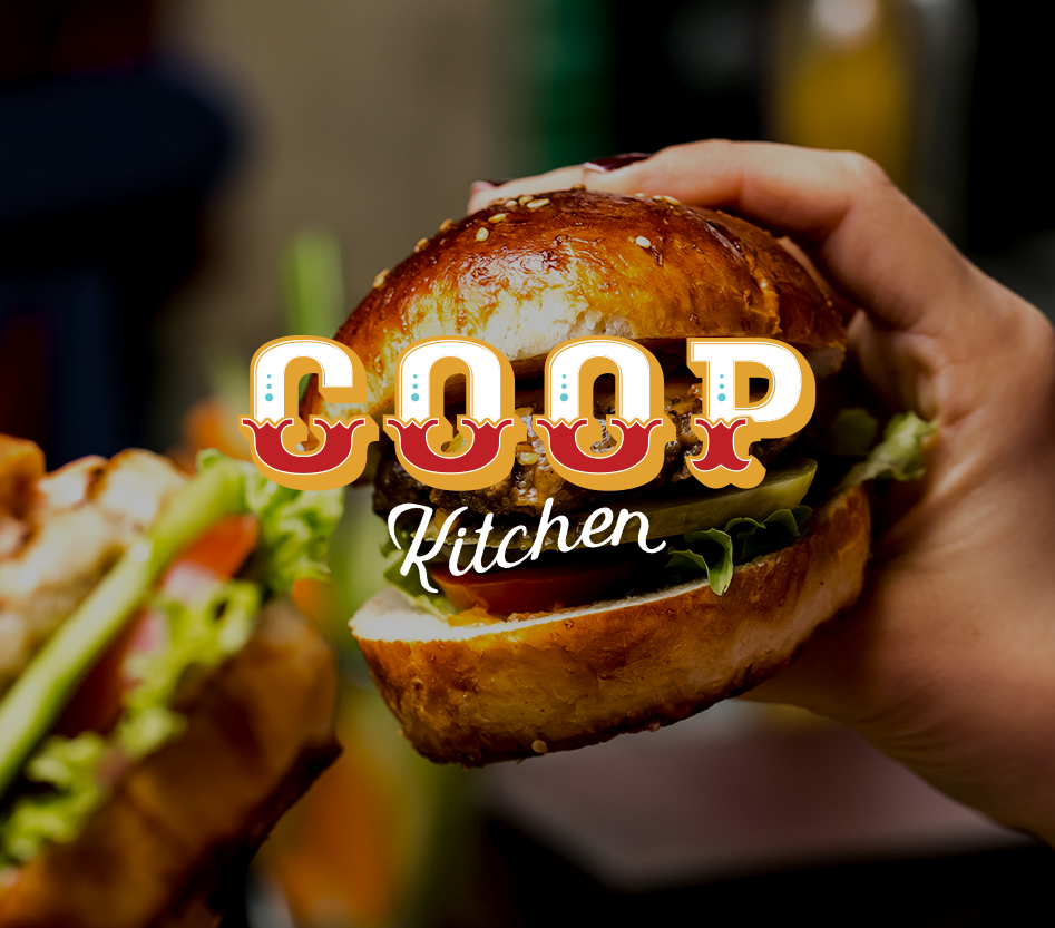 Close-up of a hand holding a burger with lettuce, tomato, pickles, and a toasted bun, with a blurred background showing the logo "Cook Kitchen".