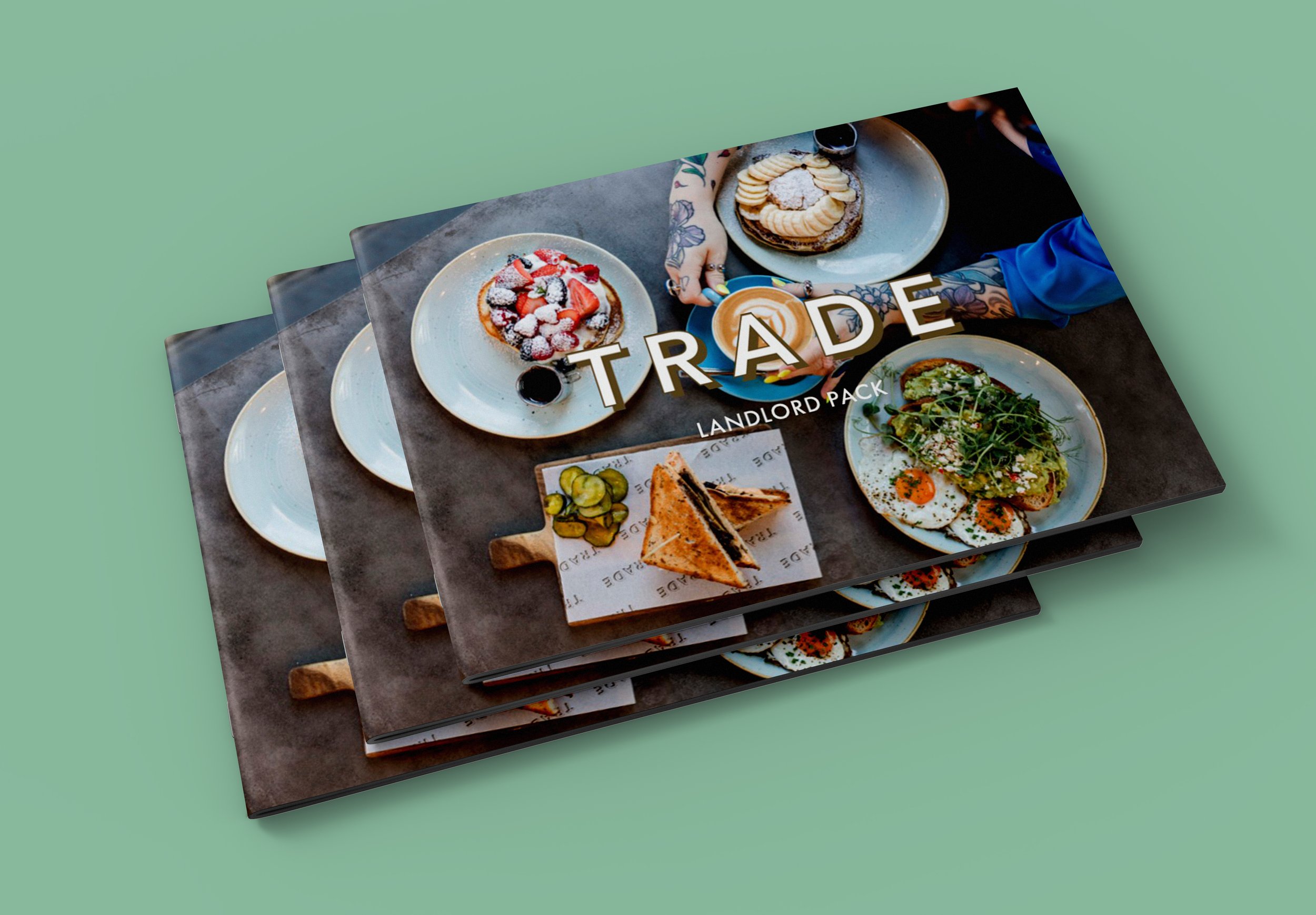 Stack of restaurant menu designs on a mint green surface, with the top menu showing a photo of various dishes including a berry-topped waffle, a pancake with banana slices, a plate of eggs with greens, and various other breakfast items.