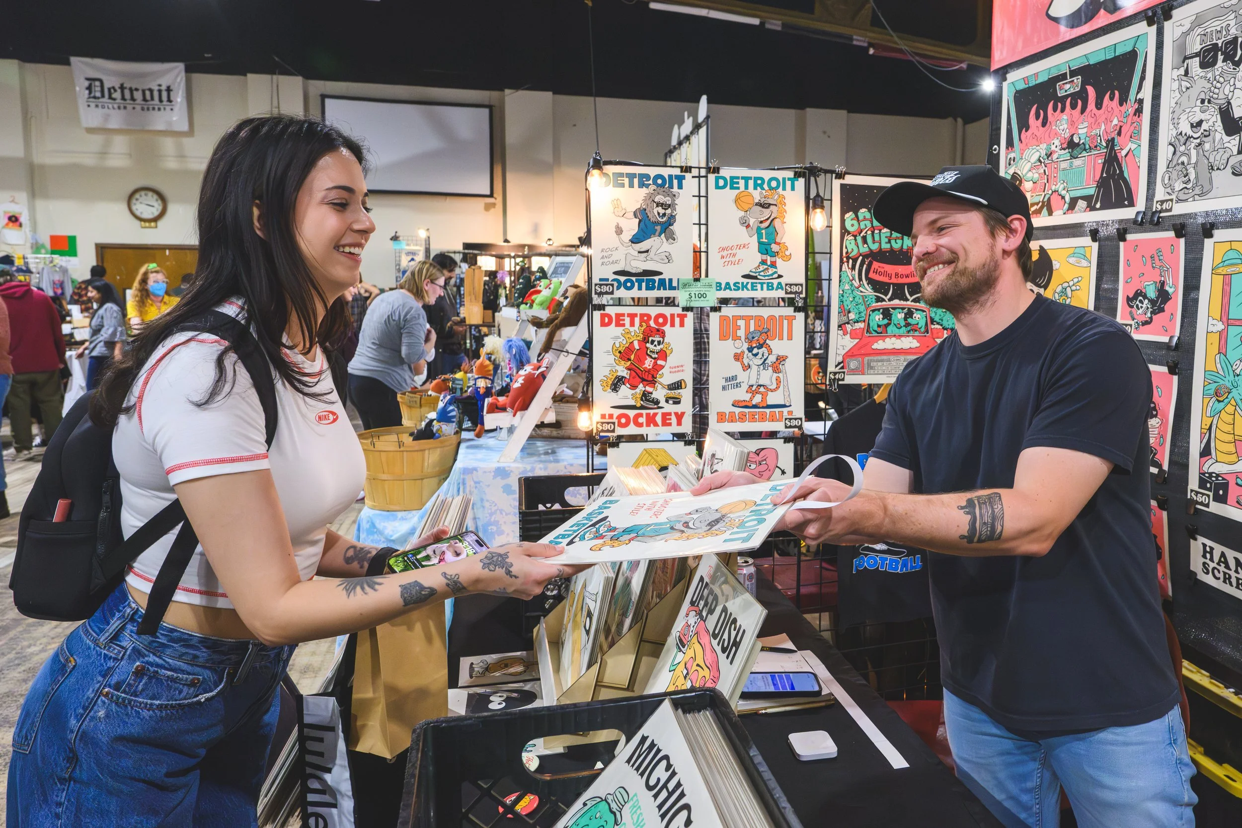 A young woman shops a booth of fun and cartoony art prints at the Detroit Urban Craft Fair, Detroit's most popular handmade and craft market.