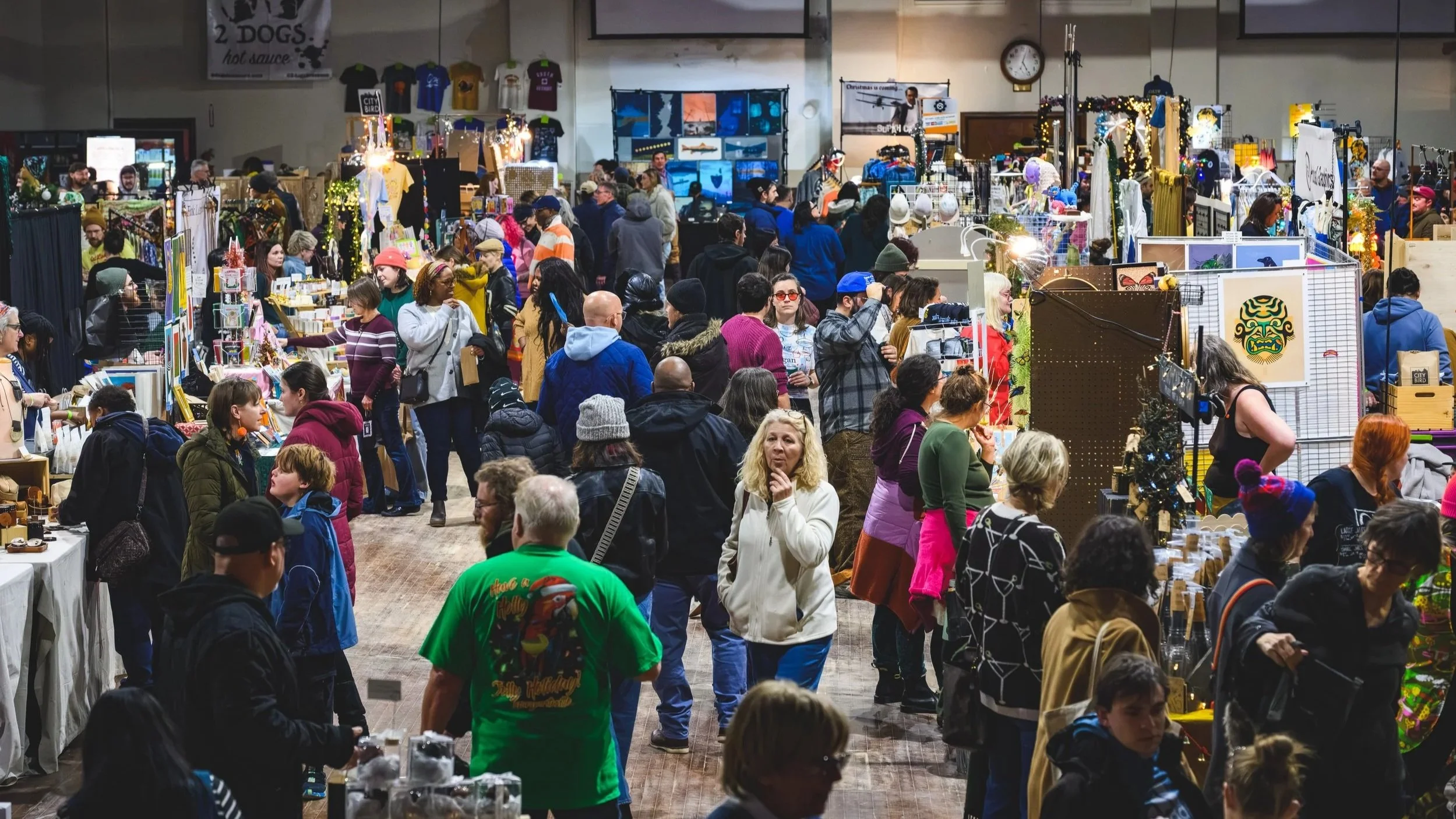 Massive crowd of people shopping at the Detroit Urban Craft Fair, with an inquisitive woman in the middle thinking of a question. Others around her shop for artwork, jewelry, clothing, and other crafts and gifts.