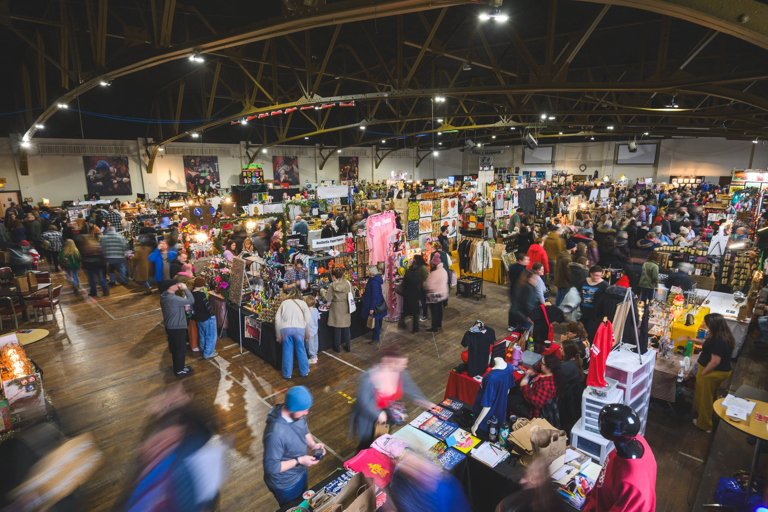 An action-packed photo of a packed scene at the Detroit Urban Craft Fair (DUCF) featuring hundreds of patrons shopping booths filled with beautiful handmade goods including toys, jewelry, gifts, and other items!