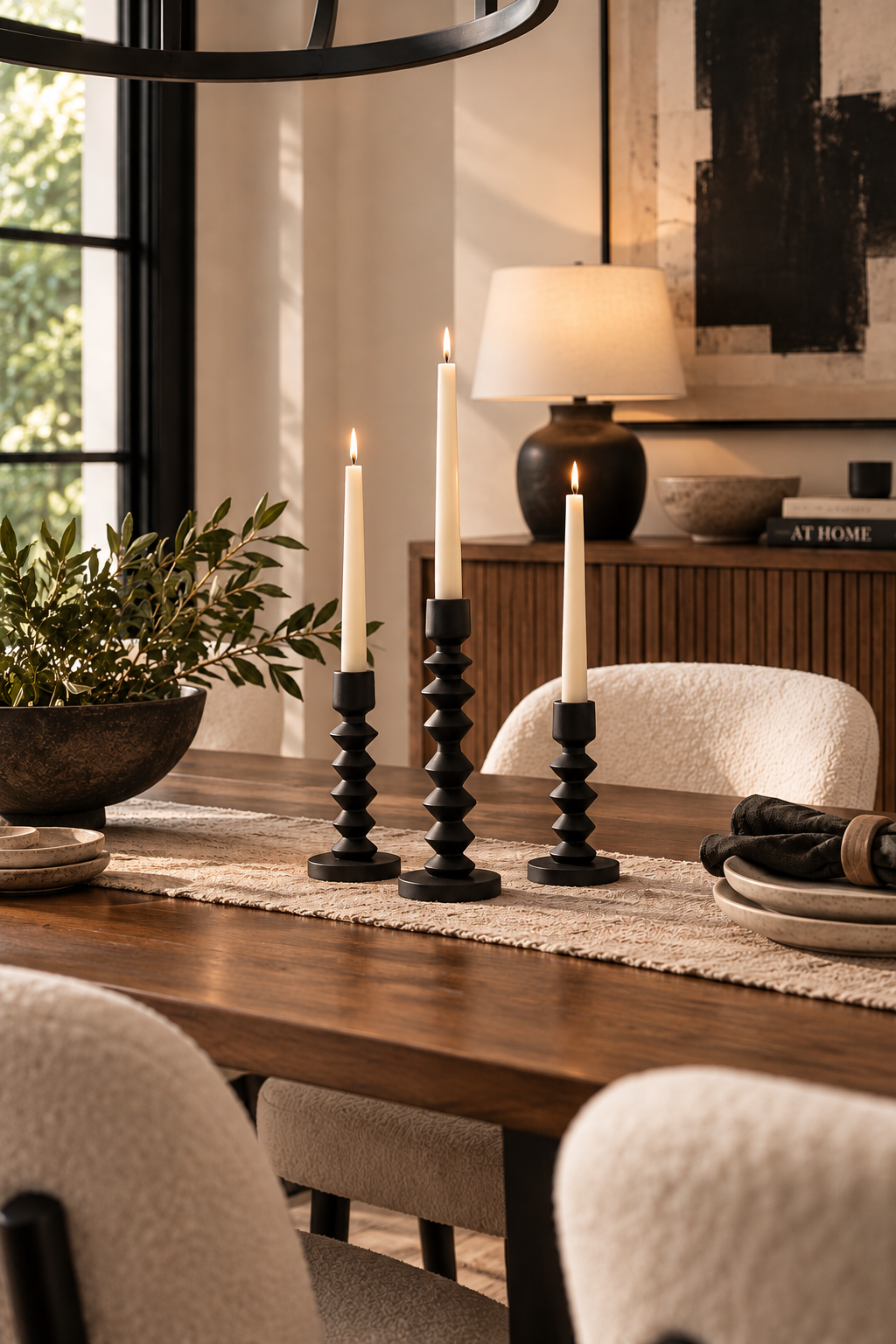 Three black tapered candles sit on top of a warm walnut dining room table with a textured table runner, cream sherpa dining room chairs