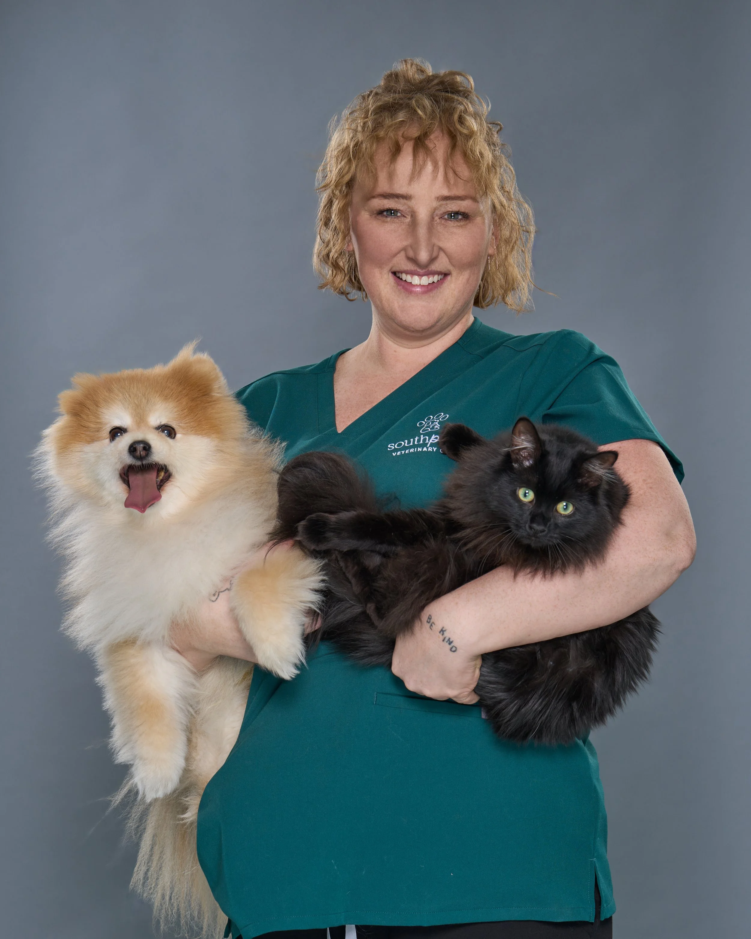 Charlene Headshot, curly hair with green scrubs holding her cat and dog