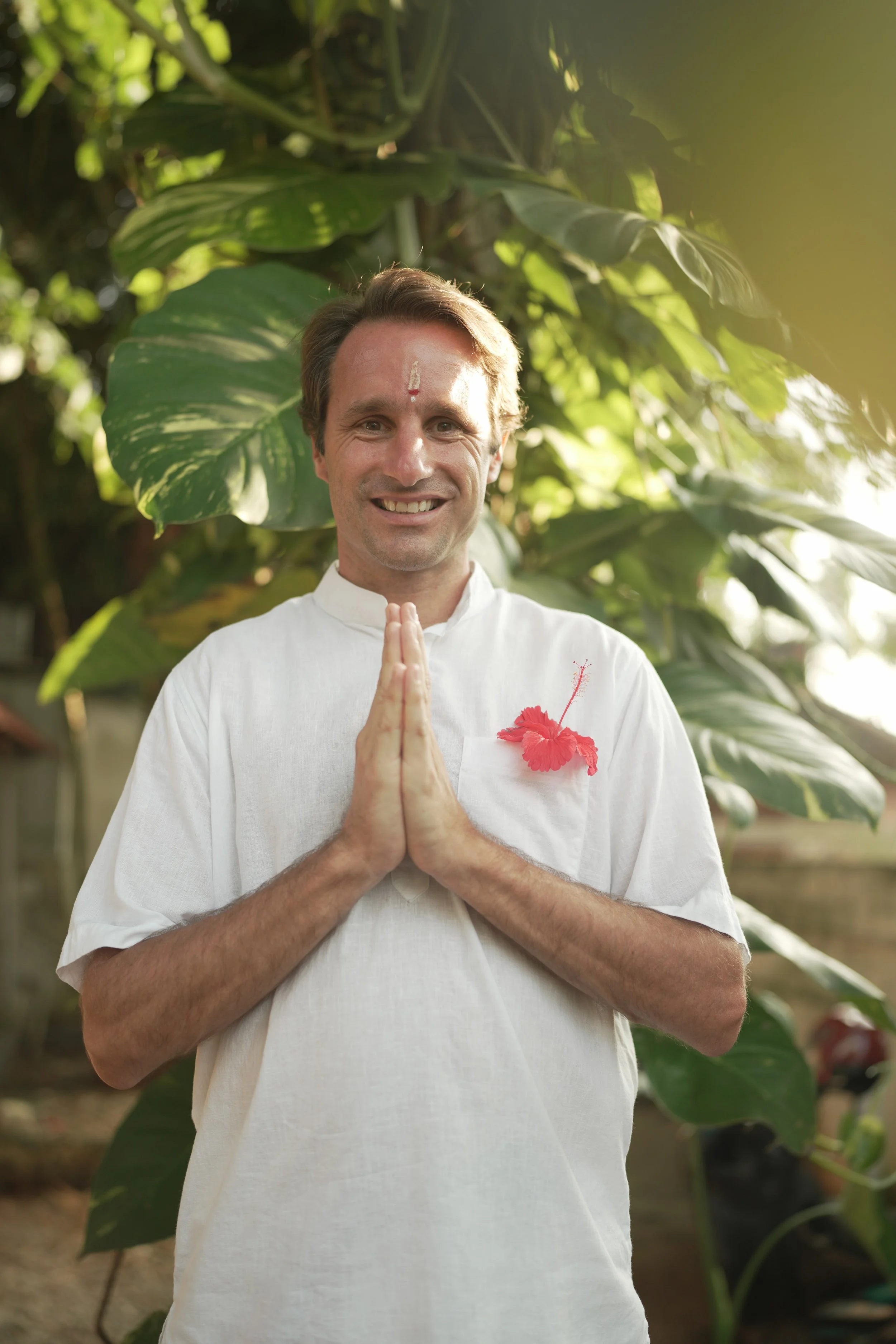 Eddy Lecas, yoga teacher, standing with hands in prayer position (anjali mudra) surrounded by greenery in India.
