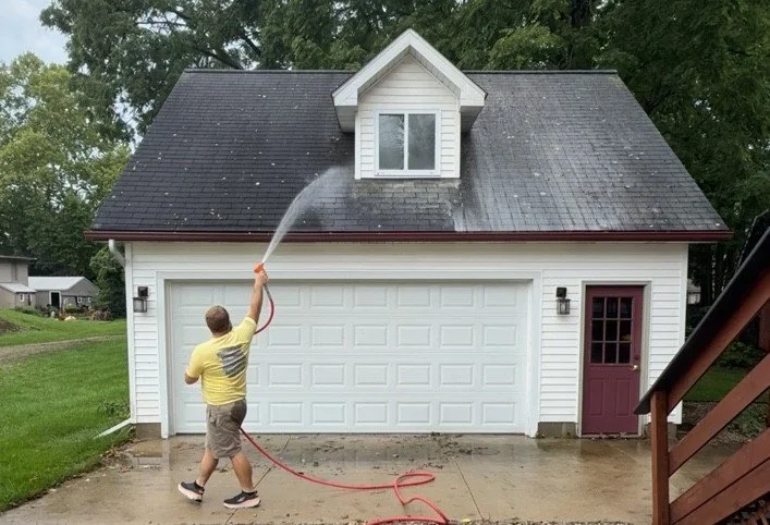 Technician applying a soft wash treatment to an asphalt shingle garage roof