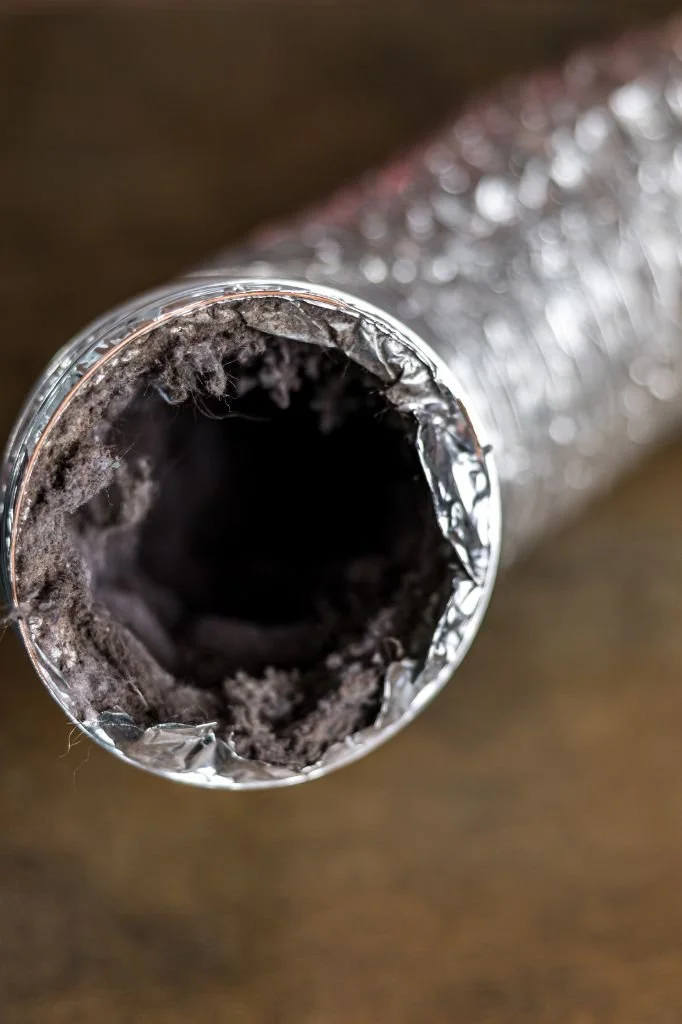 Close-up of the hollow inside of a crumpled aluminum foil-wrapped tube with black residue, on a wooden surface.