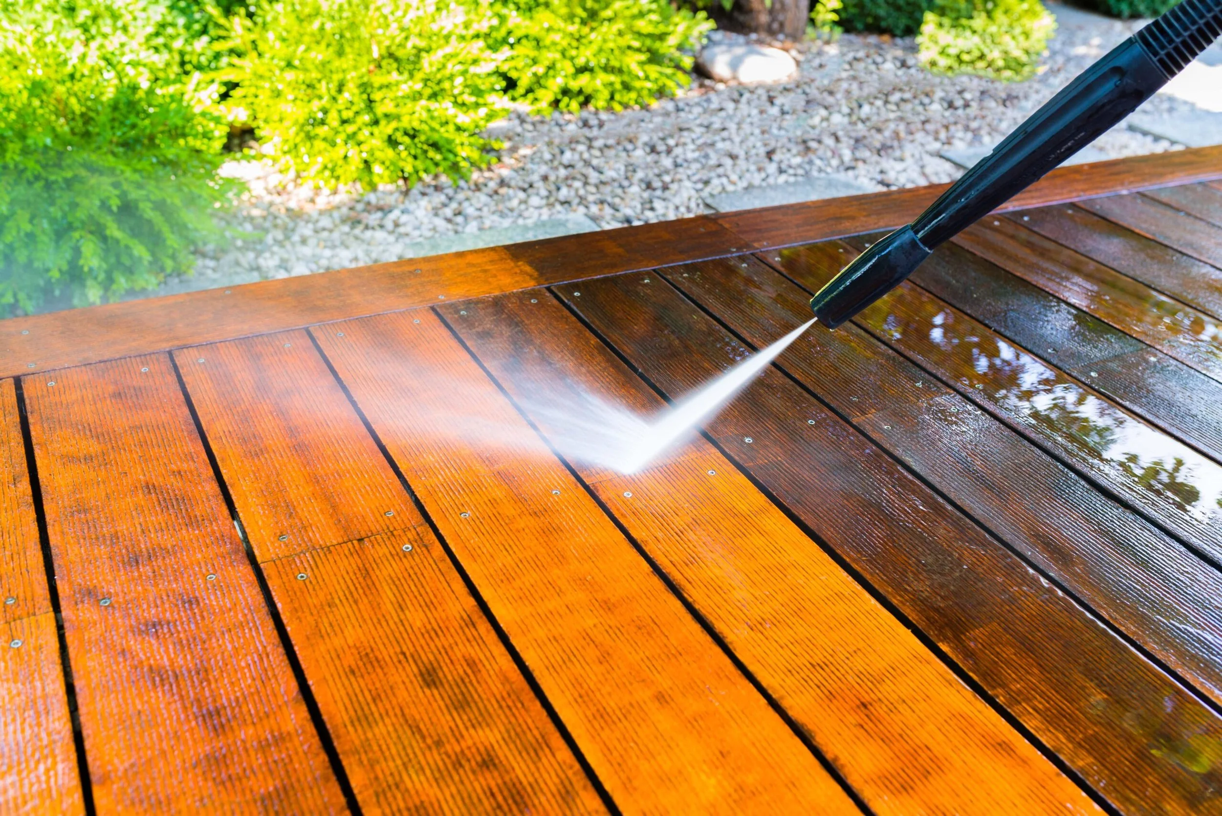A pressure washer cleaning a wooden deck with water spray.