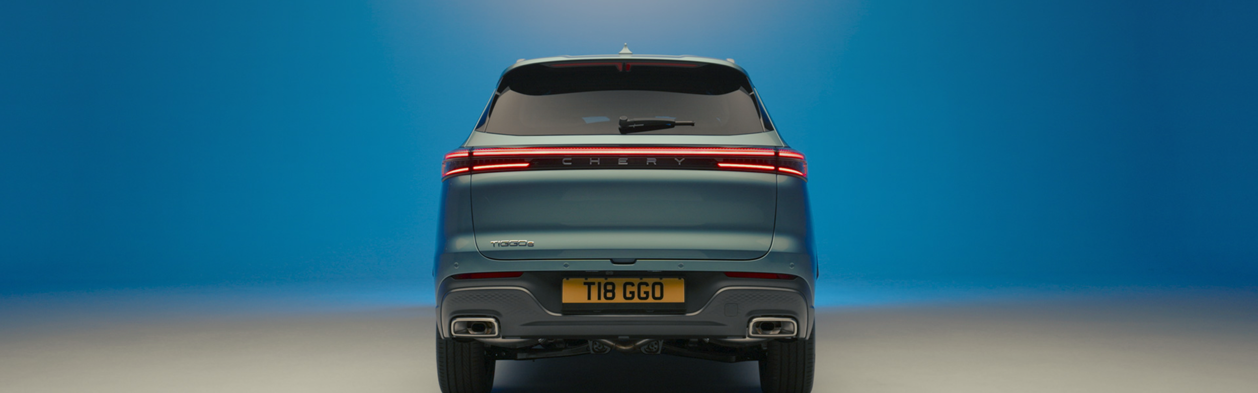 Rear view of a gray Chery Tiggo 8 GOO SUV against a blue gradient background.