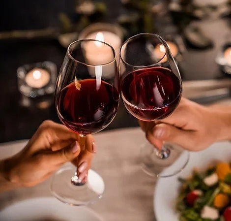 Two people clinking glasses of red wine in a toast over a dinner setting.
