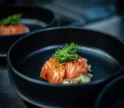 Raw salmon topped with green herbs on a black plate.