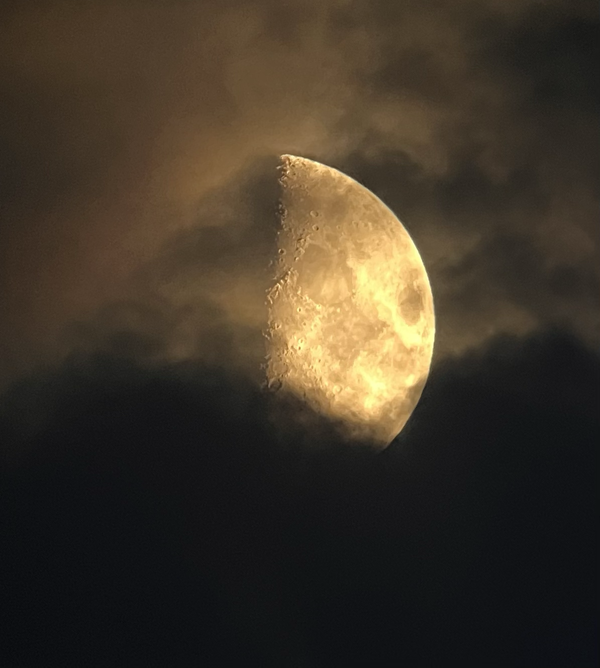 Close-up of the moon partially obscured by clouds, showing its craters and rough surface.