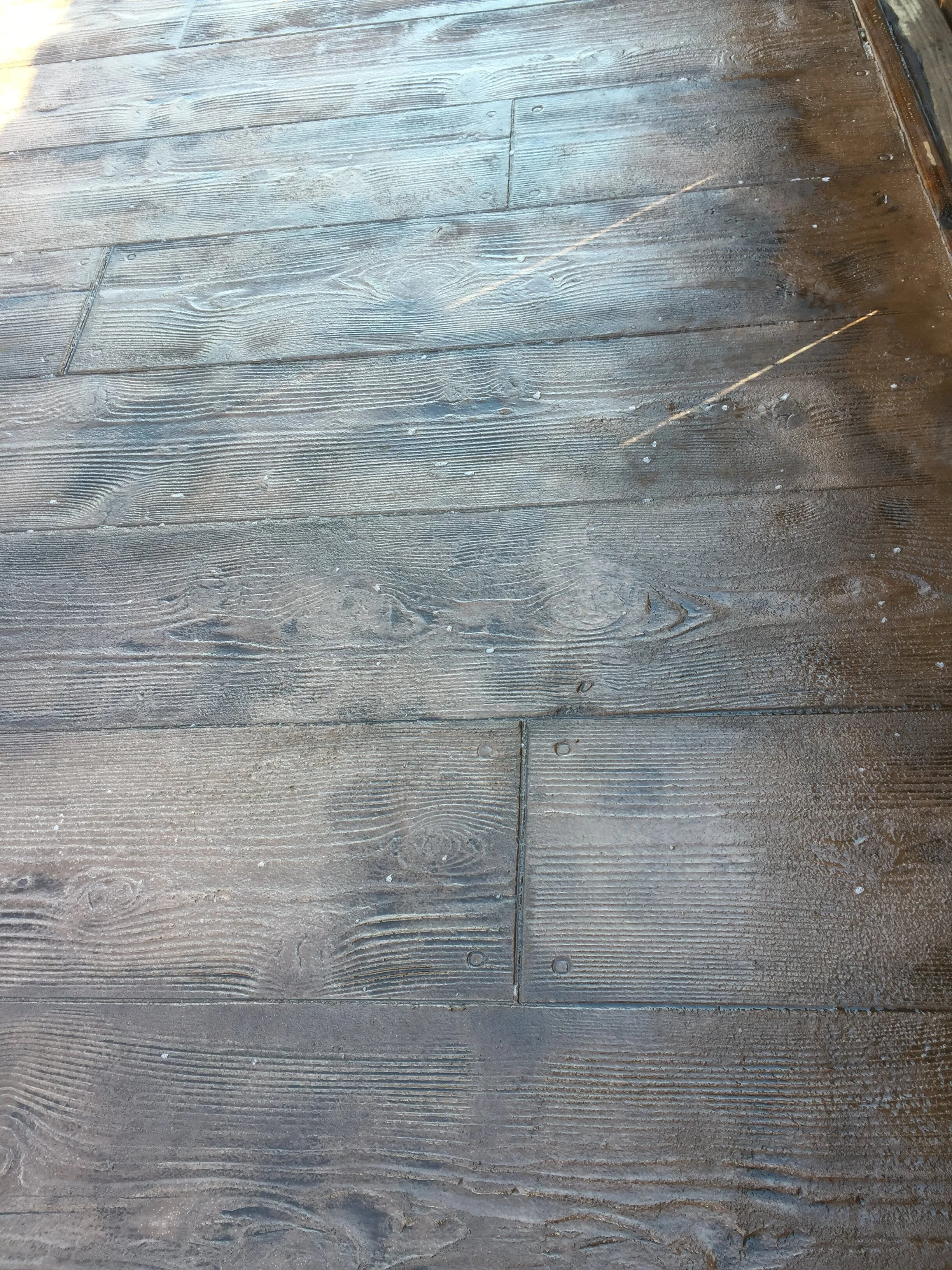 Close-up view of worn wooden planks on a floor or deck with visible grain patterns, nails, and some dust or small debris.