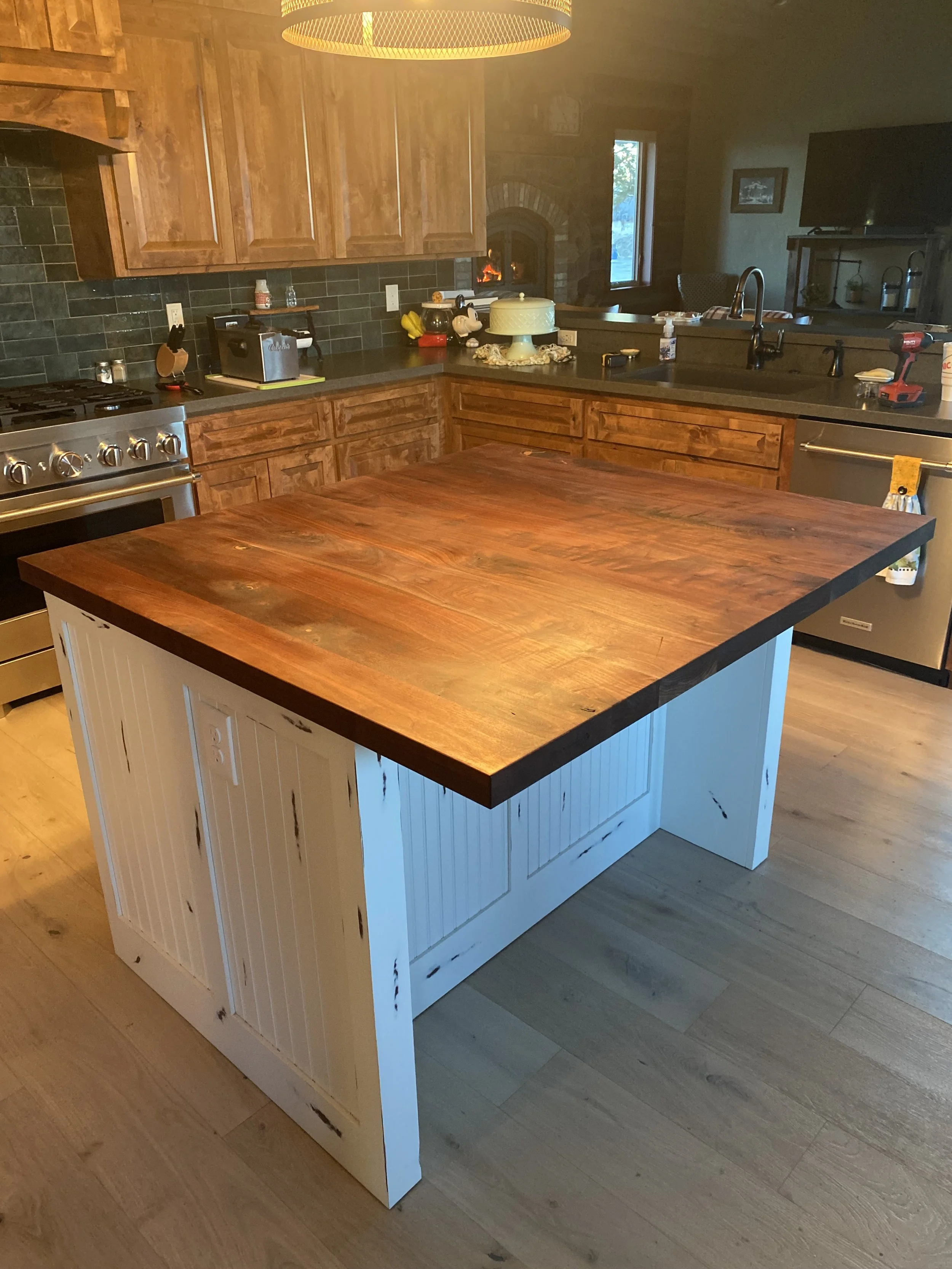 Kitchen with wooden cabinets, a white kitchen island with a wooden countertop, a stove, a sink, and a window in the background.