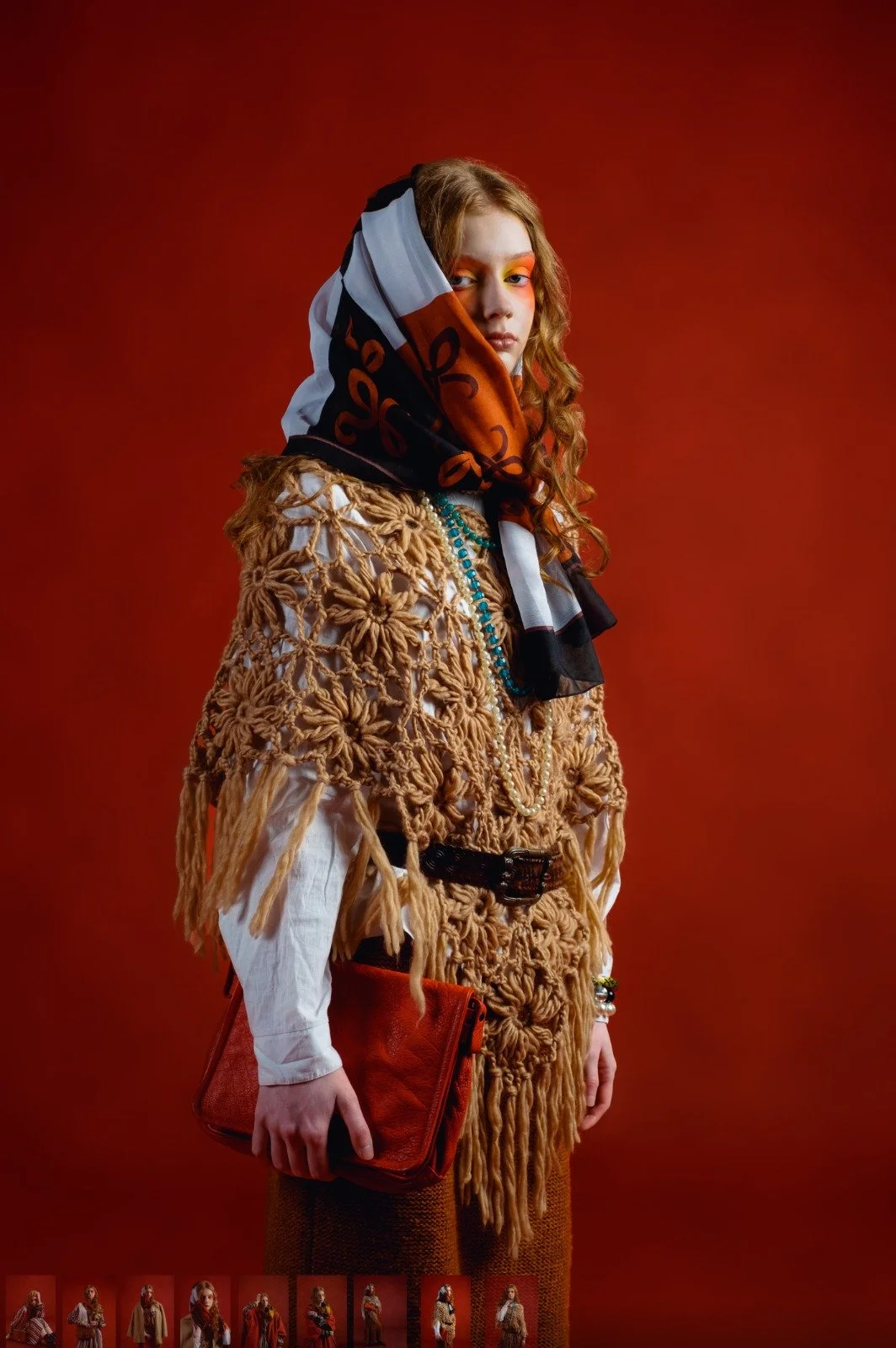Fashion model wearing a beige, chunky knit outerwear, accessorized with colorful jewelry, holding an orange clutch, with a vibrant red background.