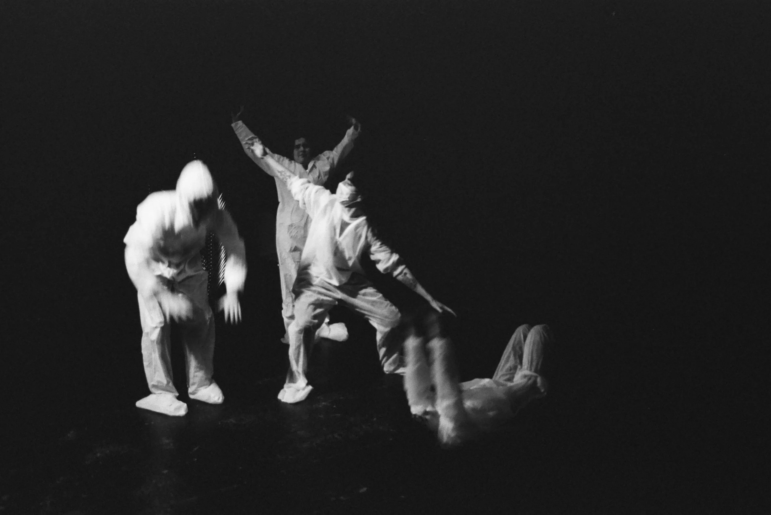 Black and white photo of a group of performers in traditional costumes, dancing or performing on stage against a dark background.