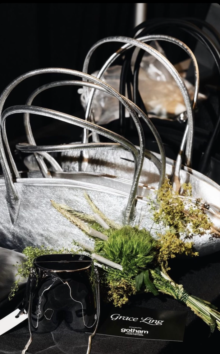 Silver metallic handbags, a black wine glass, and a bouquet of flowers on a table, with a business card reading 'Grace Ling' and 'gotham' in front.